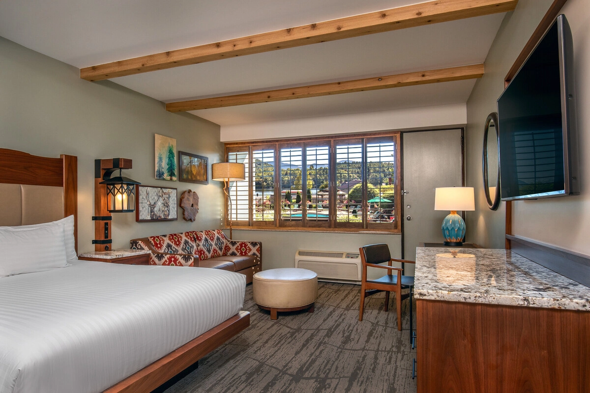 Hotel room with wooden ceiling beams, large bed with white bedspread, and seating area with patterned and leather couch
