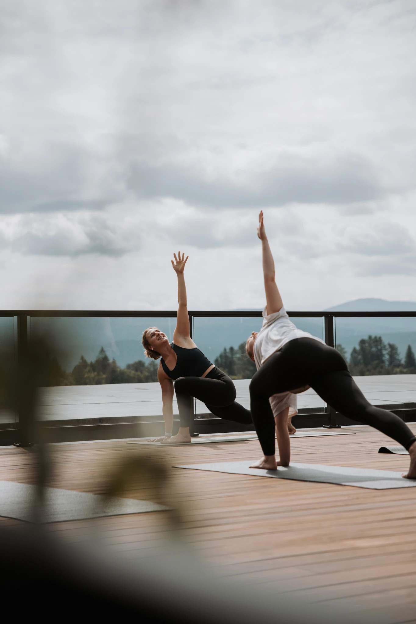 Two people practice yoga on the outdoor rooftop deck of a hotel with a lake in the background