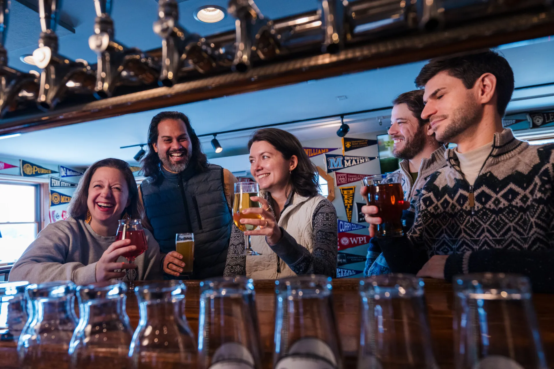Group of friends seen between taps and beer glasses enjoying pints of beer and laughing