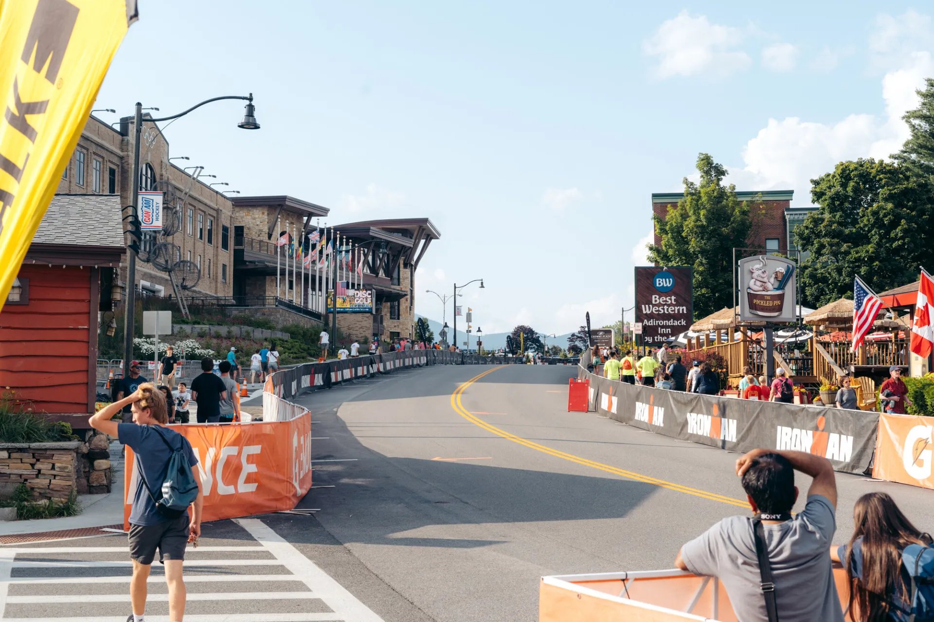 IRONMAN course in front of Conference Center at Lake Placid with branded sidewalk barriers and athletes on bikes