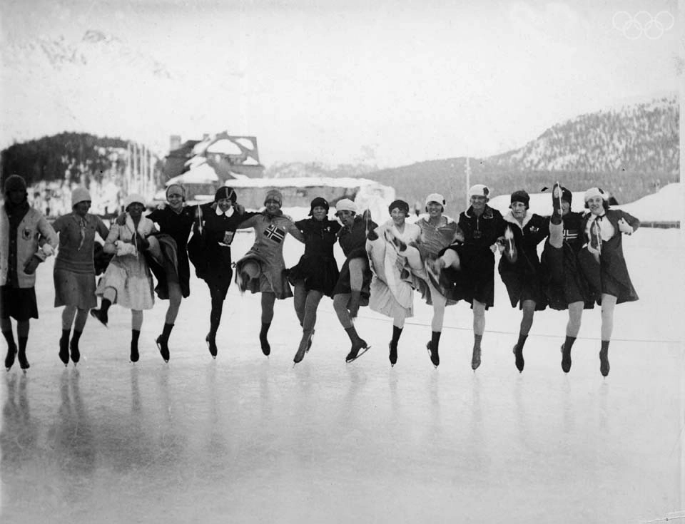 A black and white image of a group of female figure skaters leaping into the air at an outdoor rink in 1932.