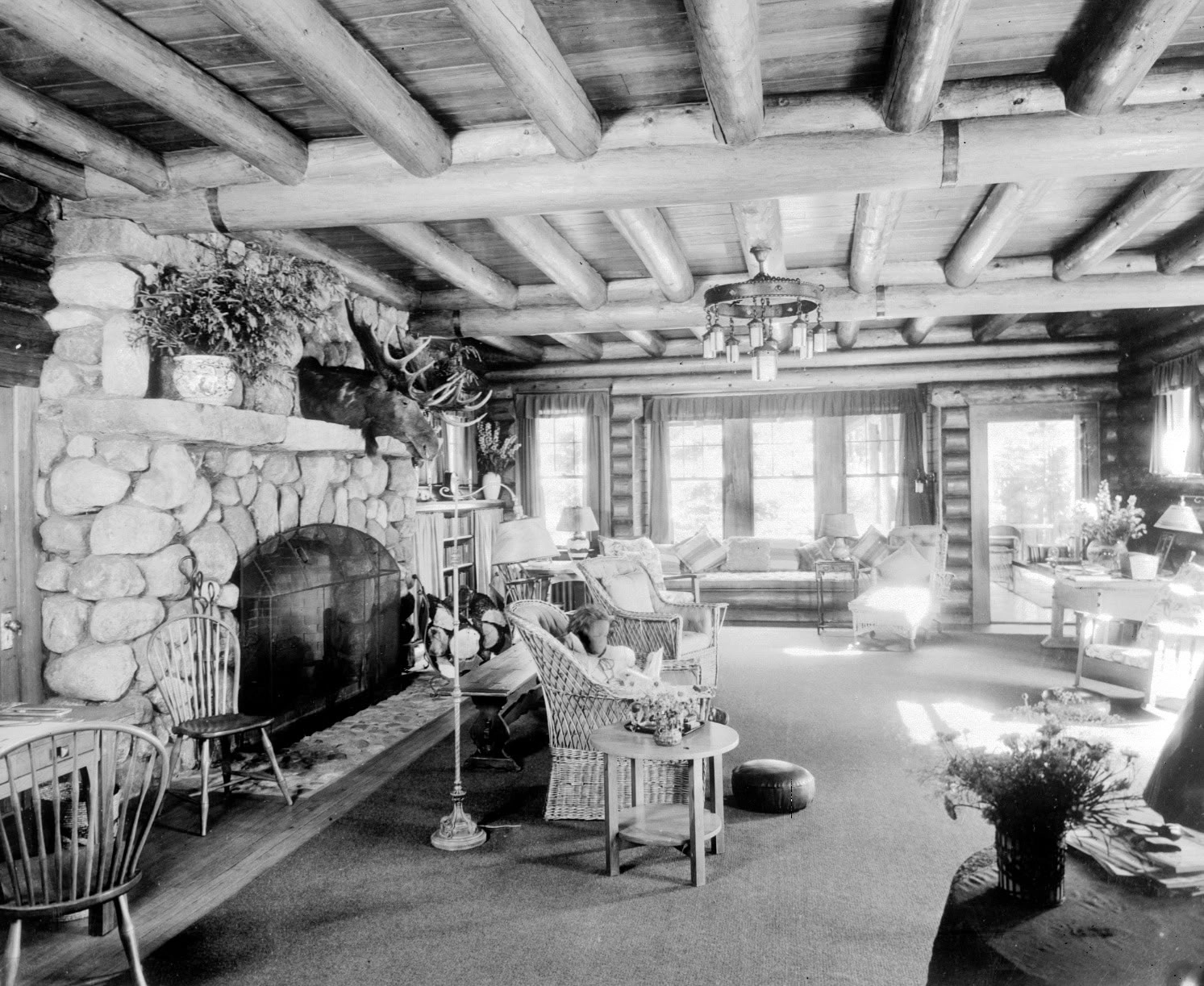 A black and white antique image of the interior of an Adirondack Great Camp living room, featuring large stone fireplace.
