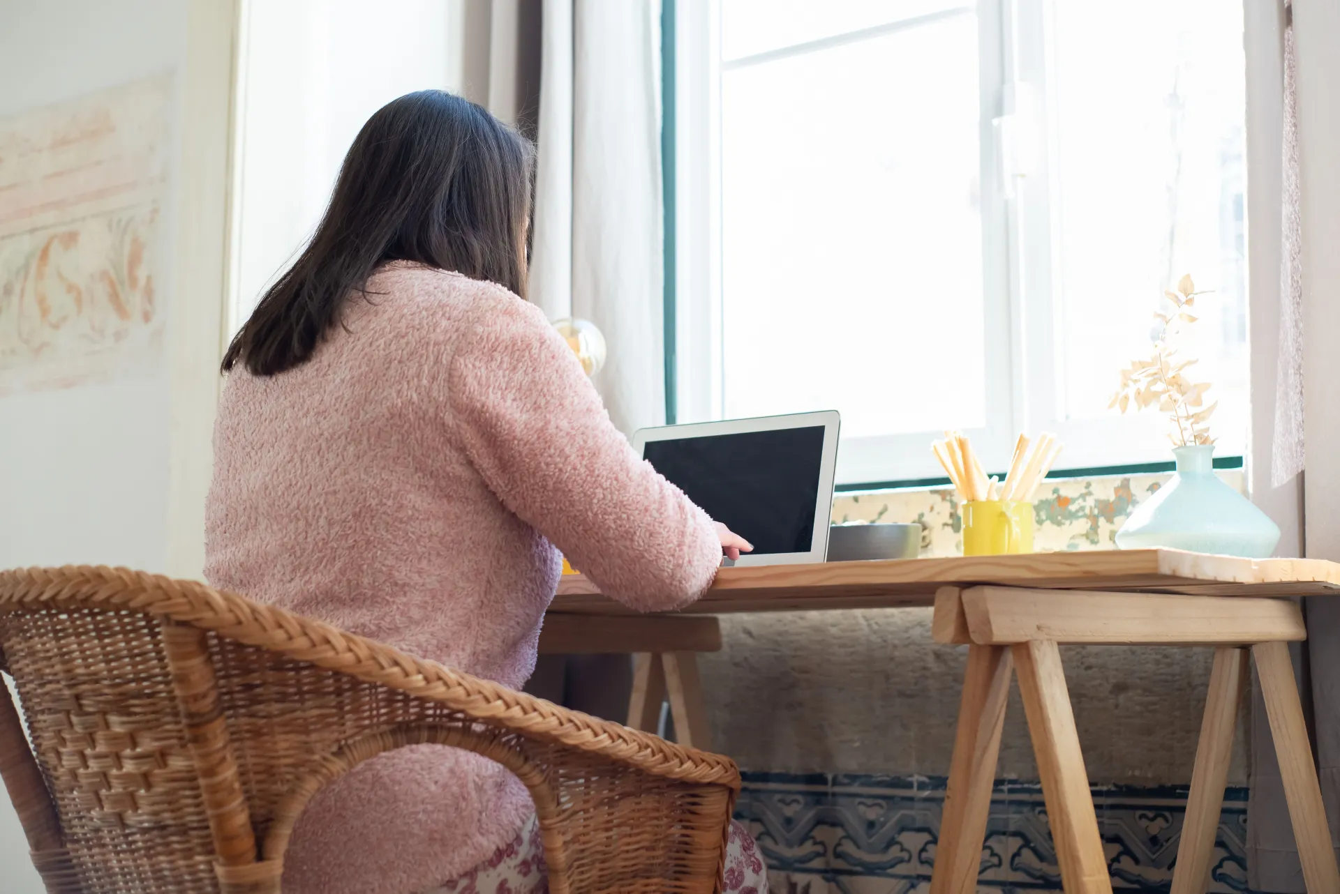 Stock image of a woman sitting at a desk turned away from the camera working on a laptop at home