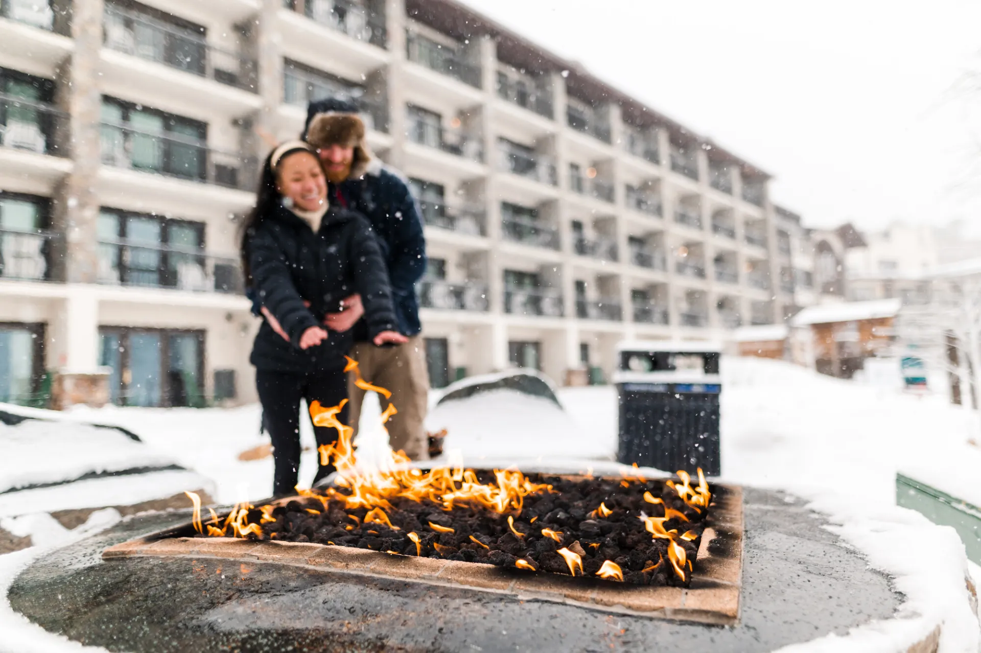 A couple standing in front of a fire during their stay in Lake Placid.