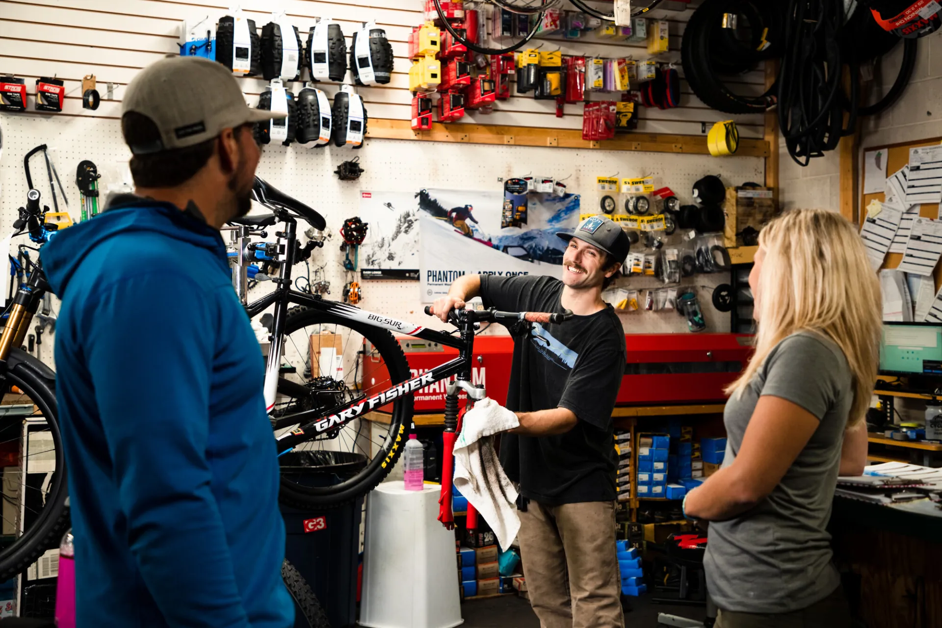 A man works on a bike while speaking to customers in a bike shop. 
