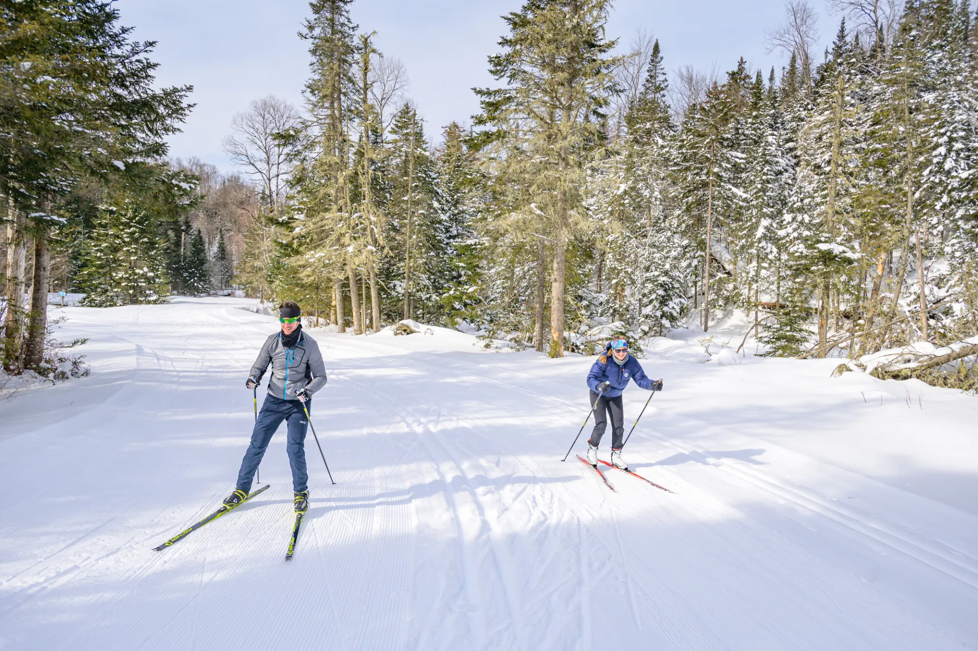 Two women cross-country ski on a wide open path in winter. 
