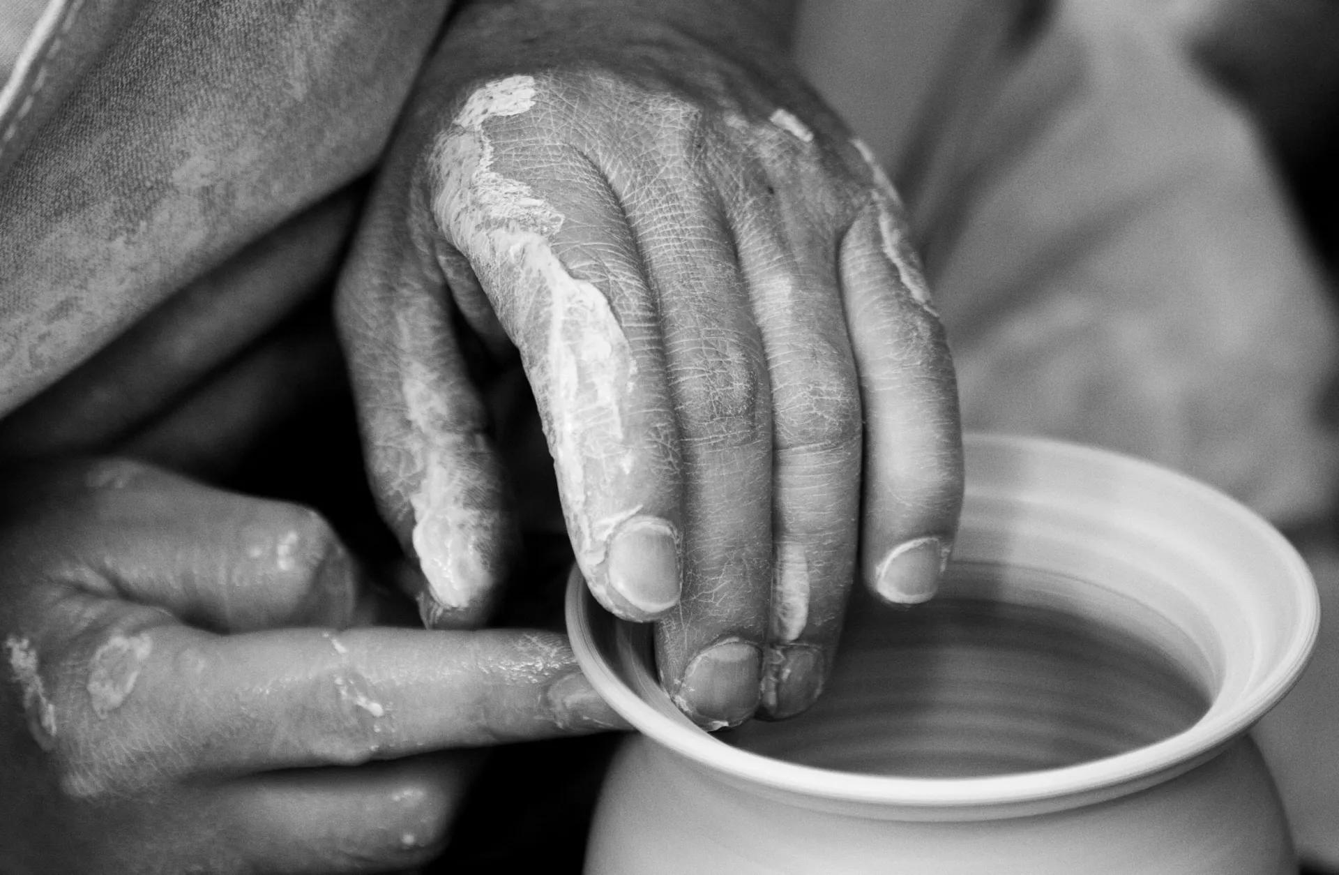 Black and white stock image of hands shaping clay pot with wet clay on hands