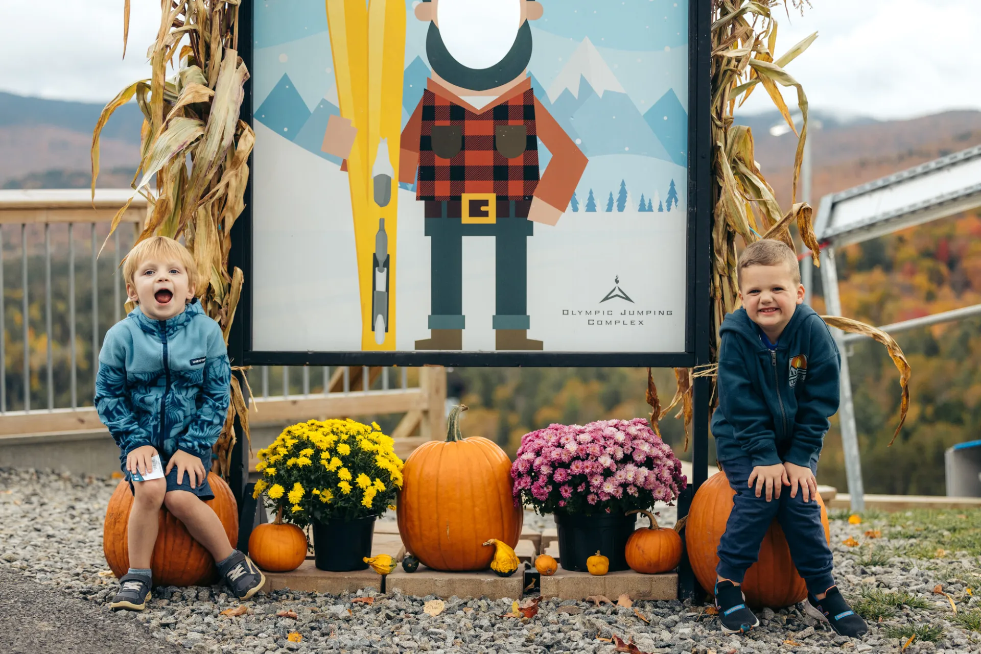 Two kids sitting next to pumpkins at a Lake Placid event.