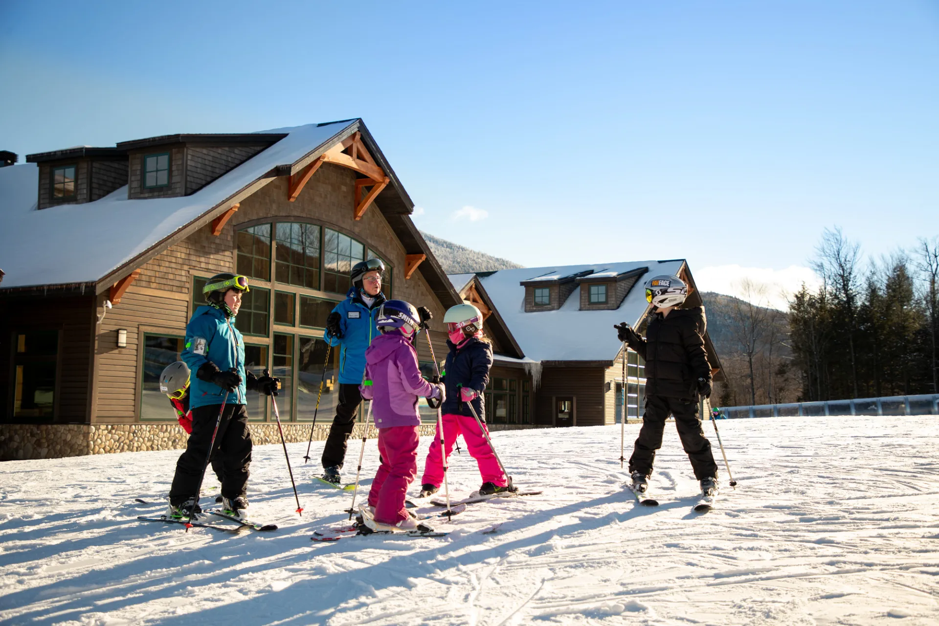 Five children taking a ski lesson with an instructor in front of the lodge at Whiteface Mountain.