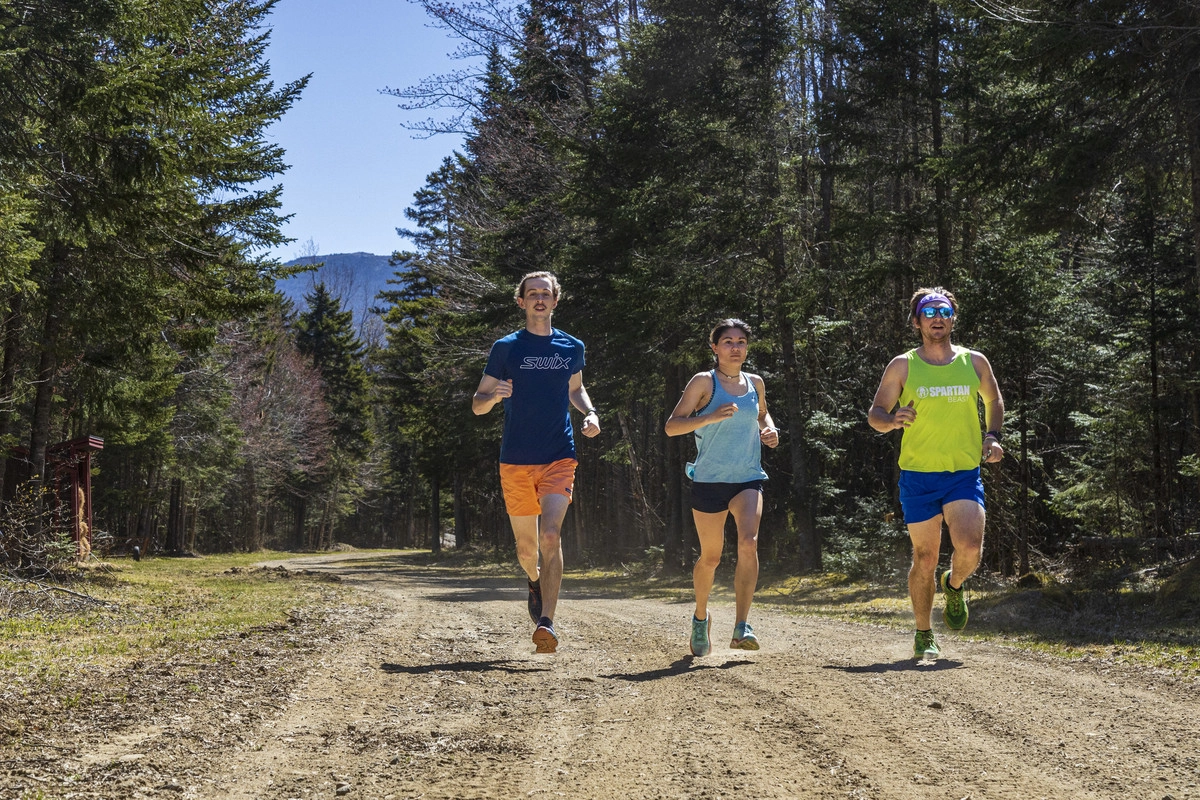 Three people jogging on a dirt path through the ski trails at mt van hoevenberg in the summer.