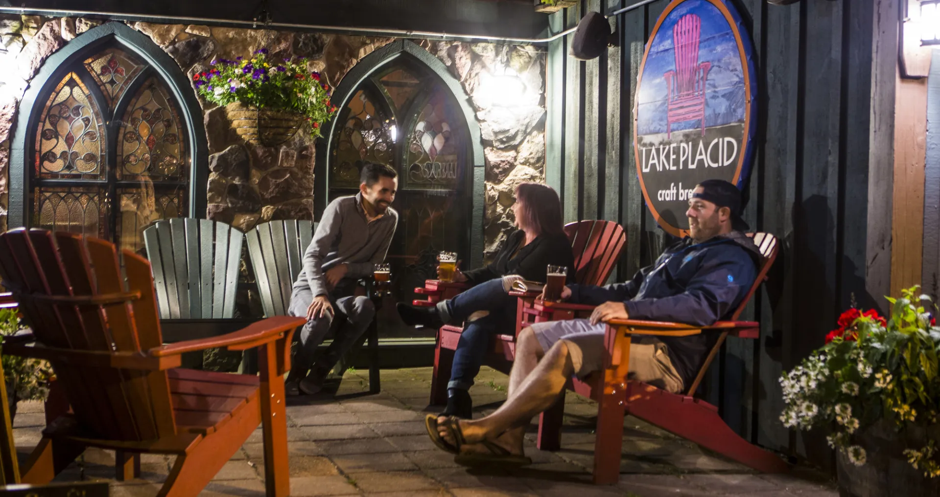 Three people socialize in Adirondack chairs at the Lake Placid Pub &amp; Brewery.