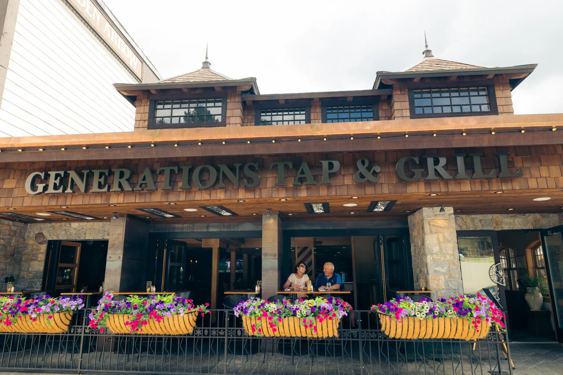 Senior couple sits at table on outdoor deck of restaurant with colorful flower boxes in front of them