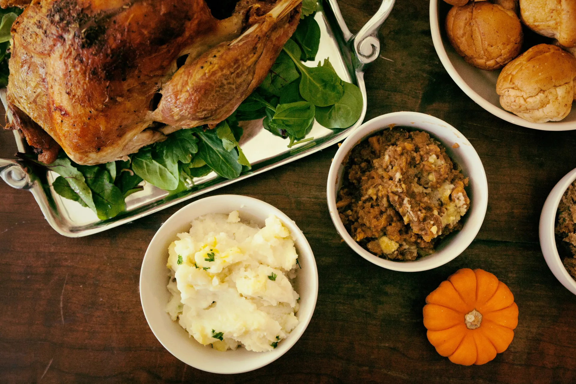 Stock image of a turkey on a platter and bowls of Thanksgiving sides on a wooden table