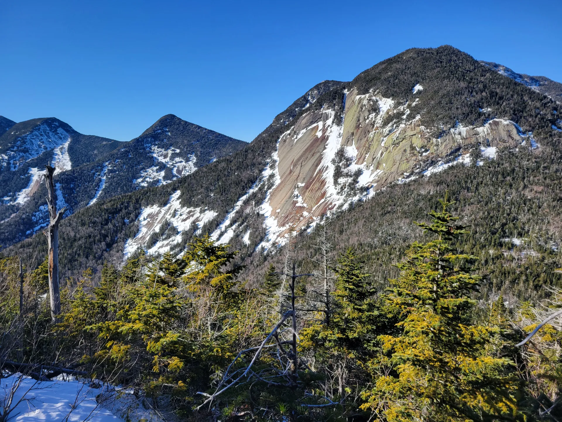 The view of mountains with large rock slabs with some snow on them.