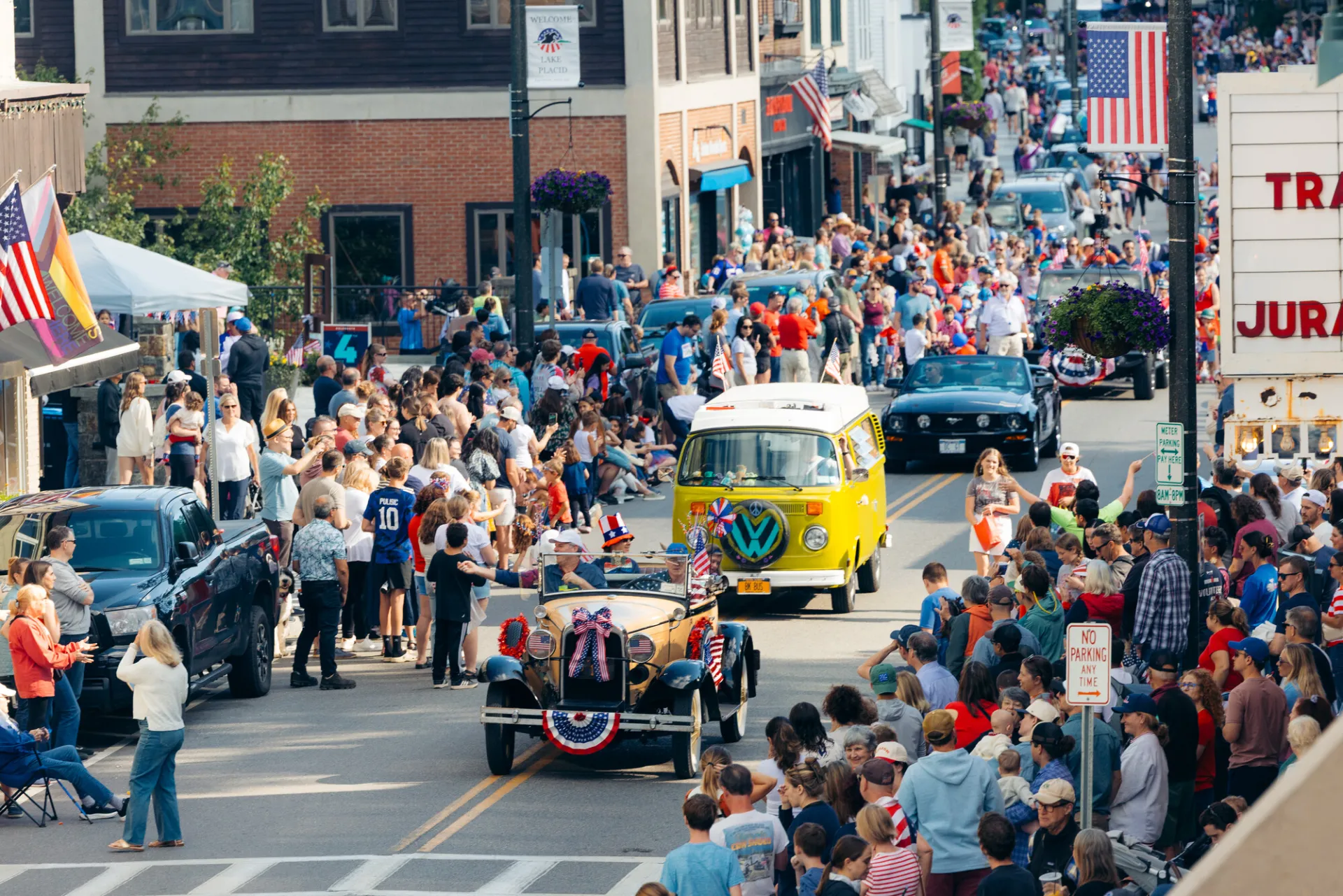 A festive Independence Day parade proceeds down a flag-lined Main Street in Lake Placid, featuring vintage cars.