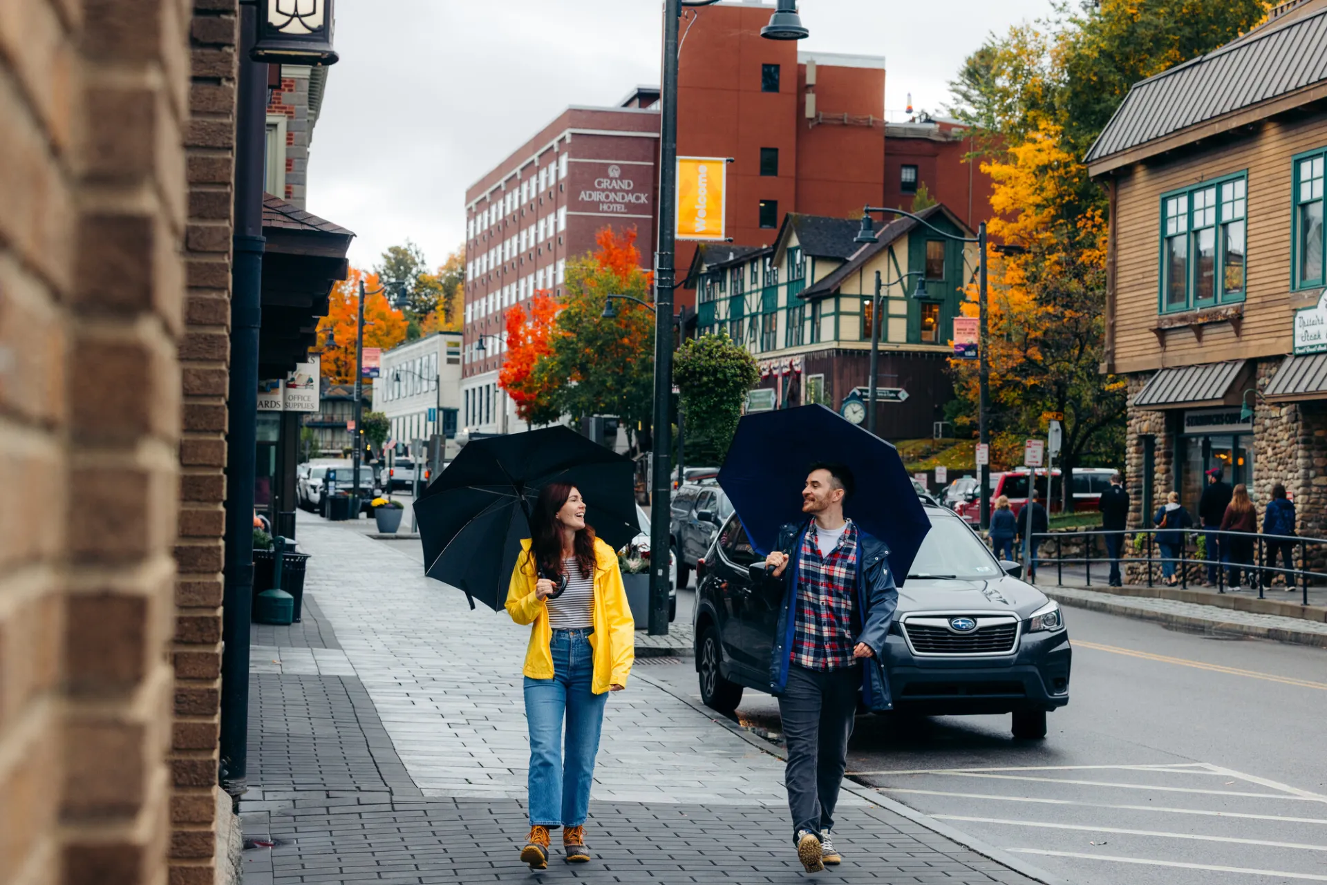 A man and woman walk in the center of a small town with umbrellas on a rainy fall day.