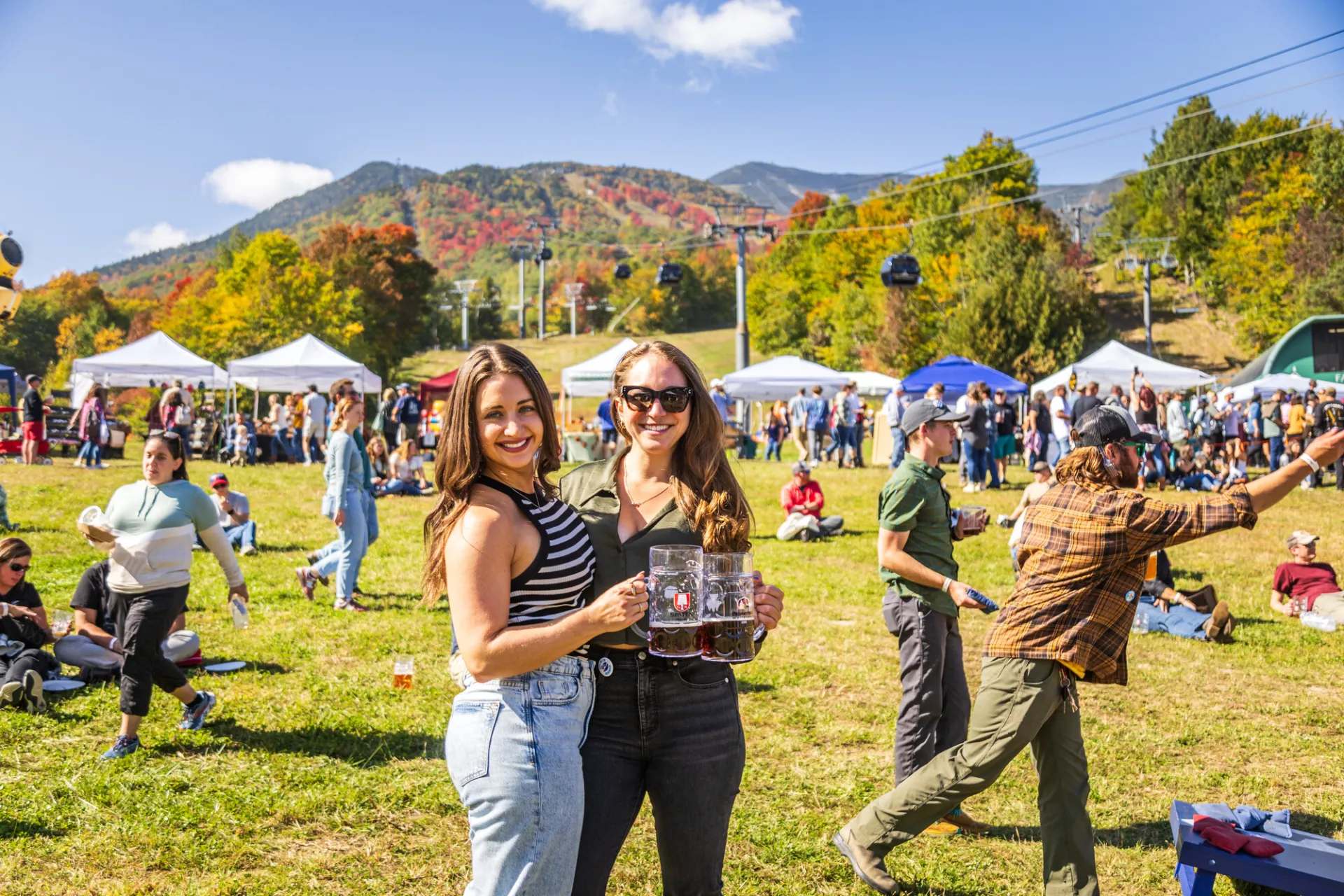 Two women standing with drinks at an outdoor fall event in Lake Placid.