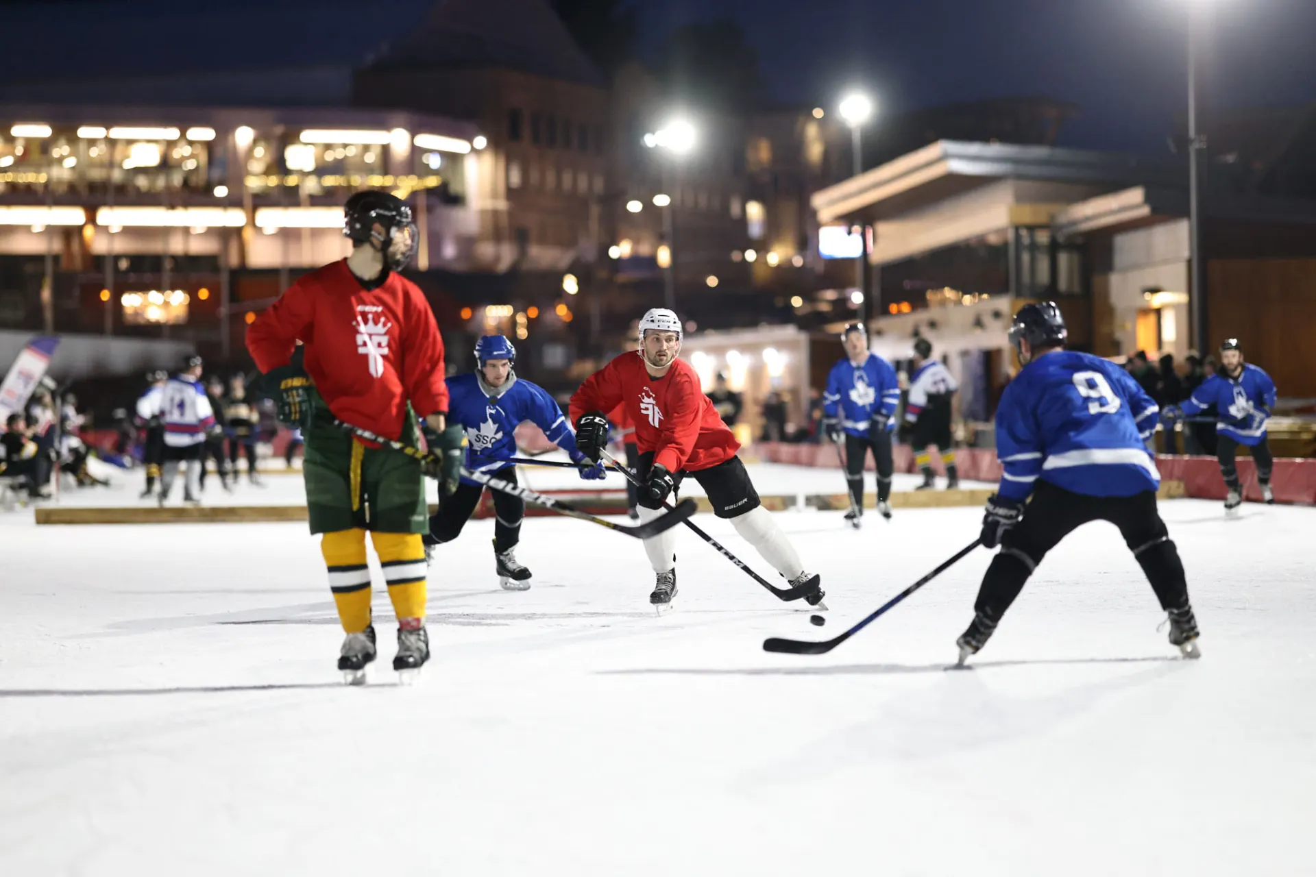 Hockey players in red and blue jerseys compete on the ice of the Olympic Oval under the lights at night