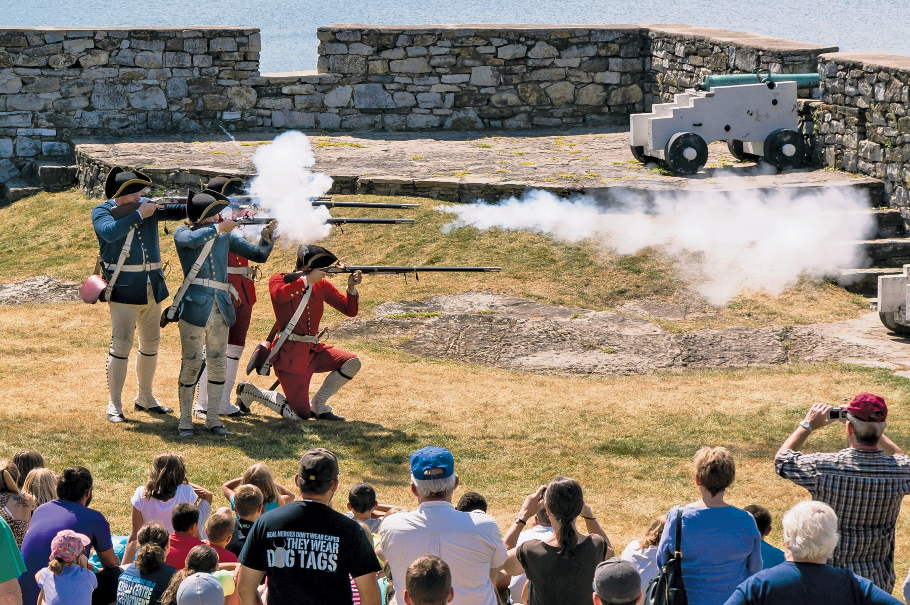 Reenactment performers fire muskets in front of a gathered crowd of on lookers.