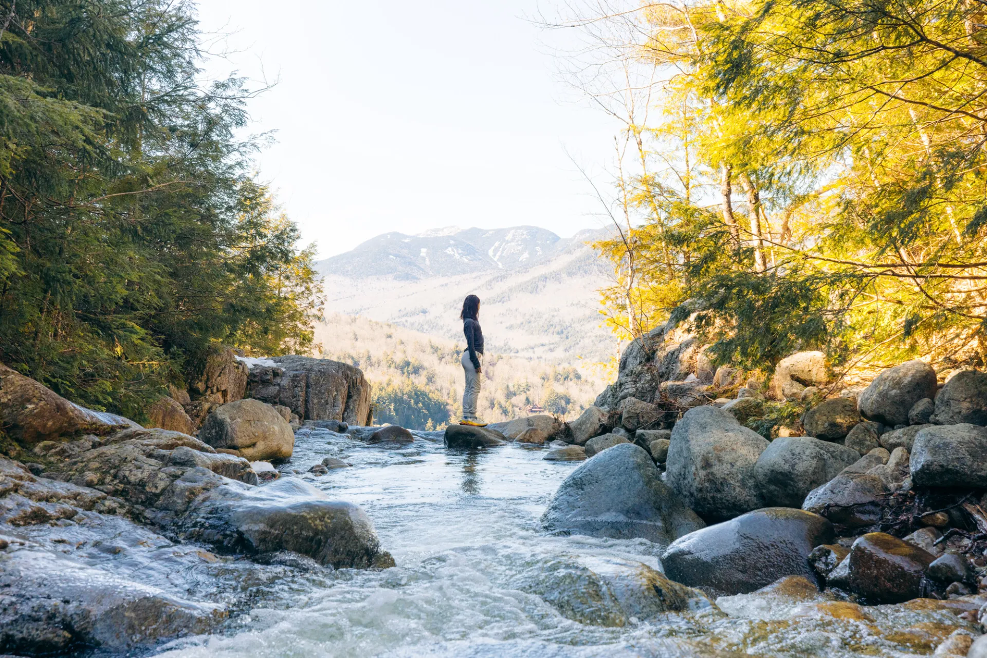 A hiker standing on a rock while crossing over a small river.