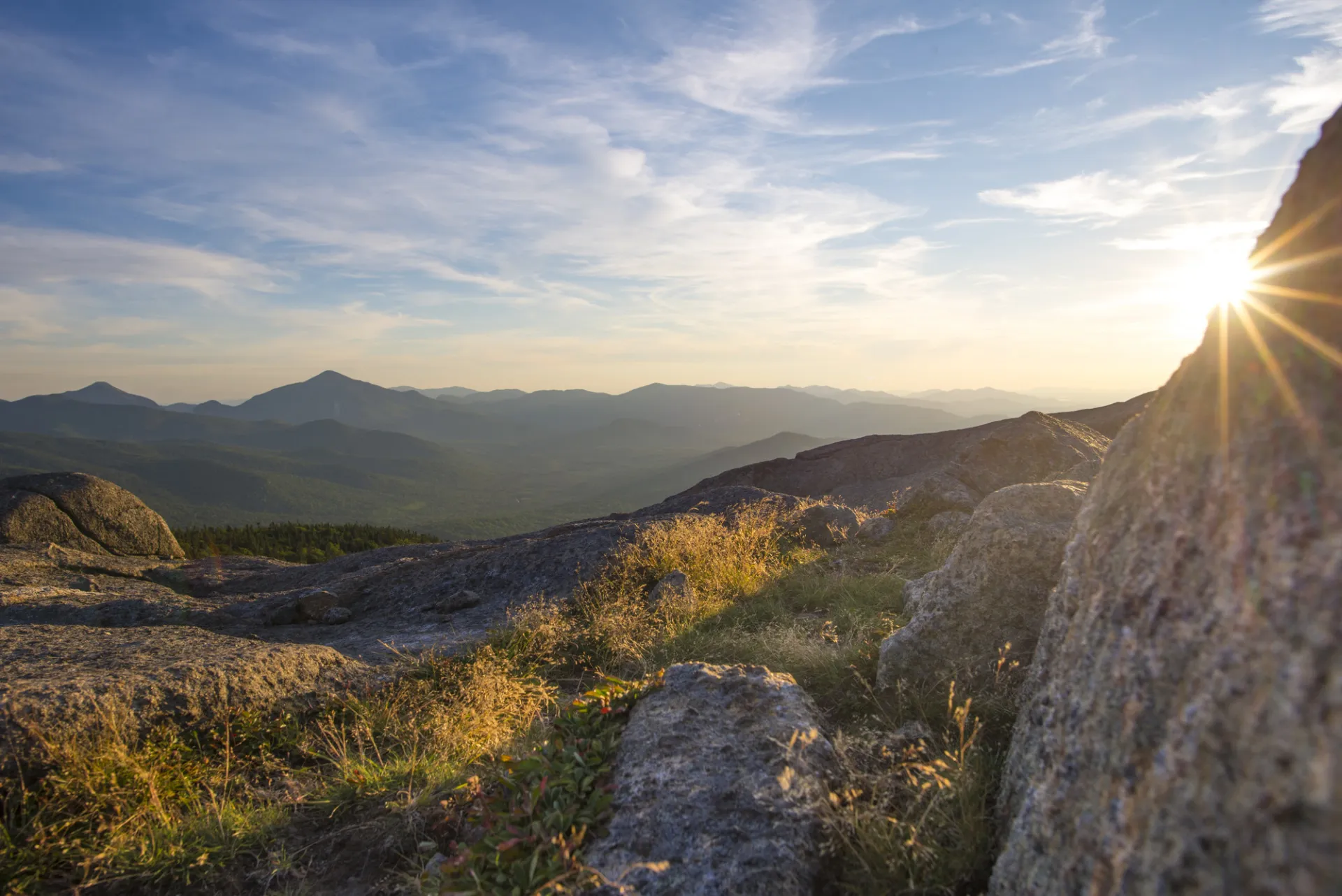 View from mountain summit with sun peaking out from behind a large rock
