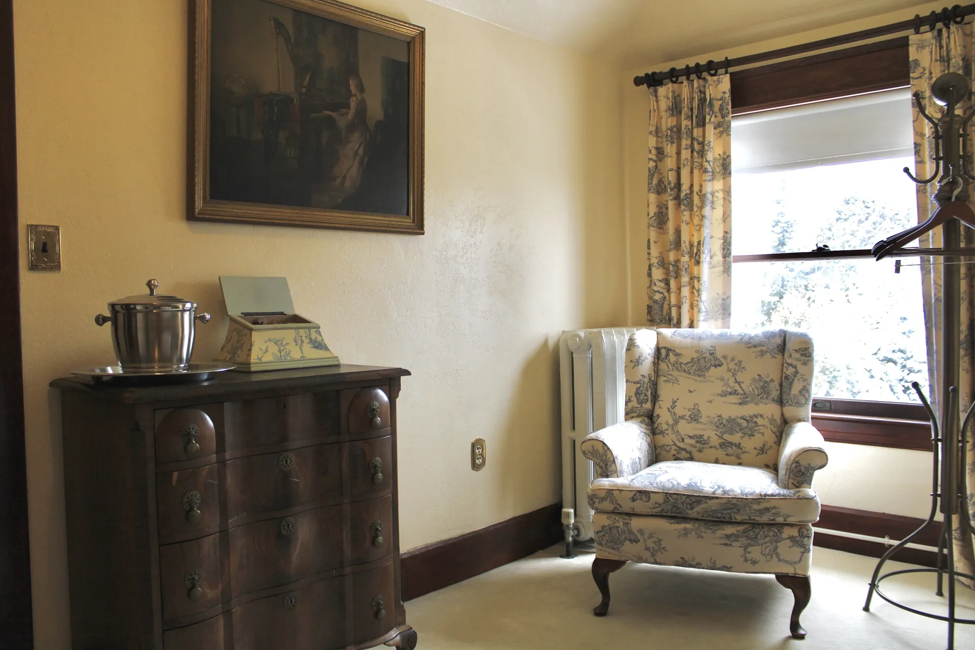 A patterned arm chair in the corner with dark furniture and a large window.