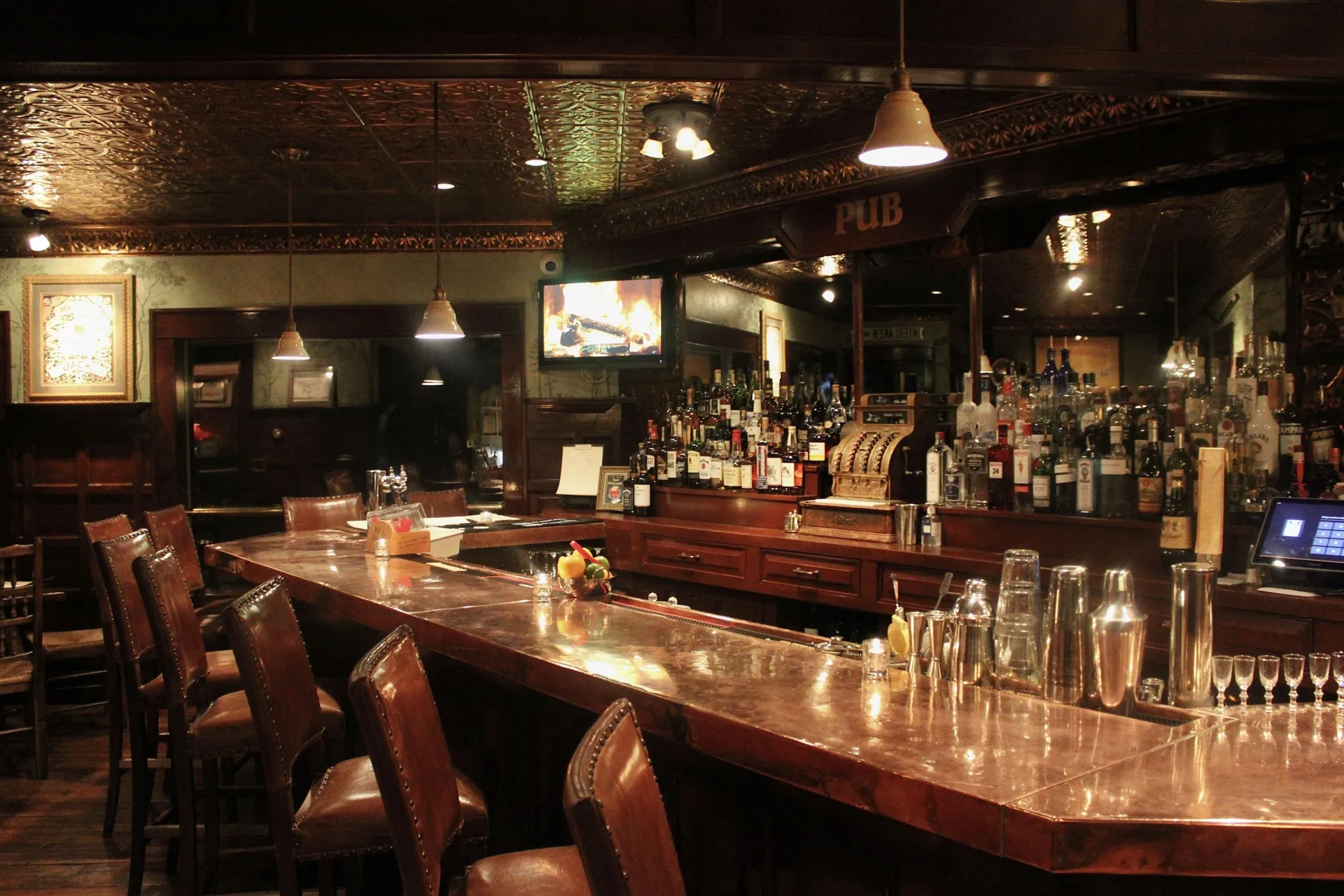 A dark and moody bar with lush leather stools and tin ceiling.