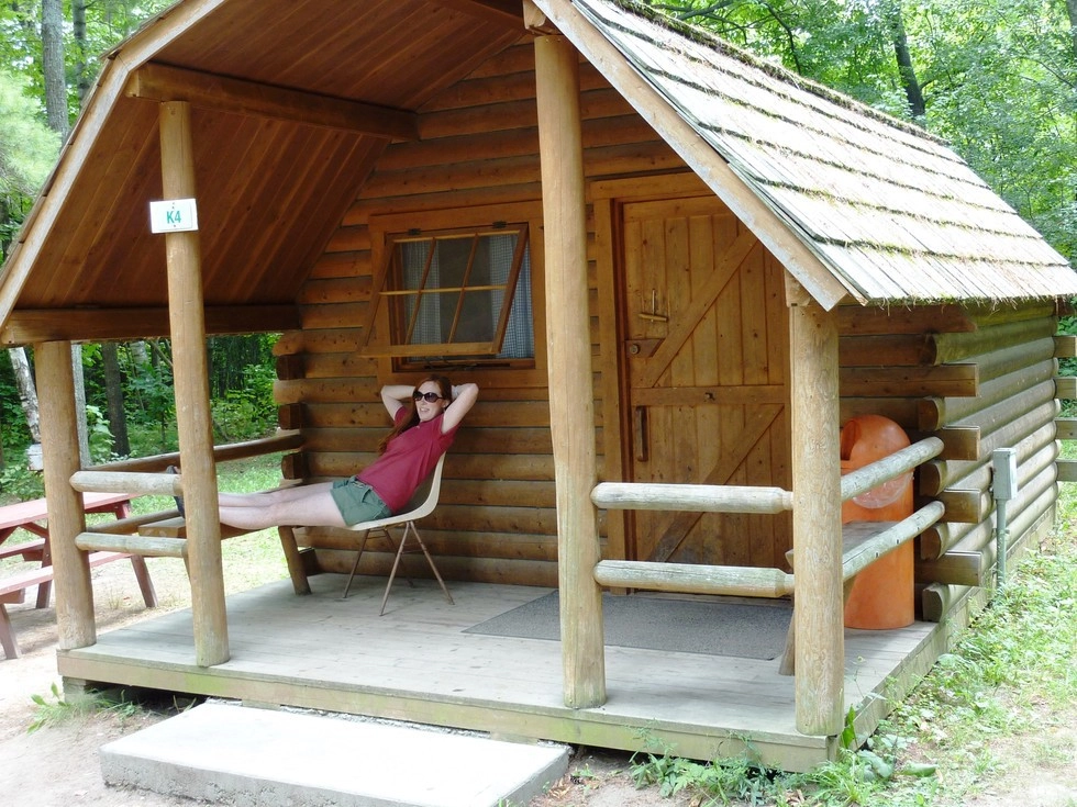 A camper lounges on the covered porch of a cabin.