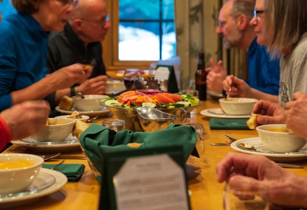 People seated at wooden dining table eating with family-style meal laid out on center of table