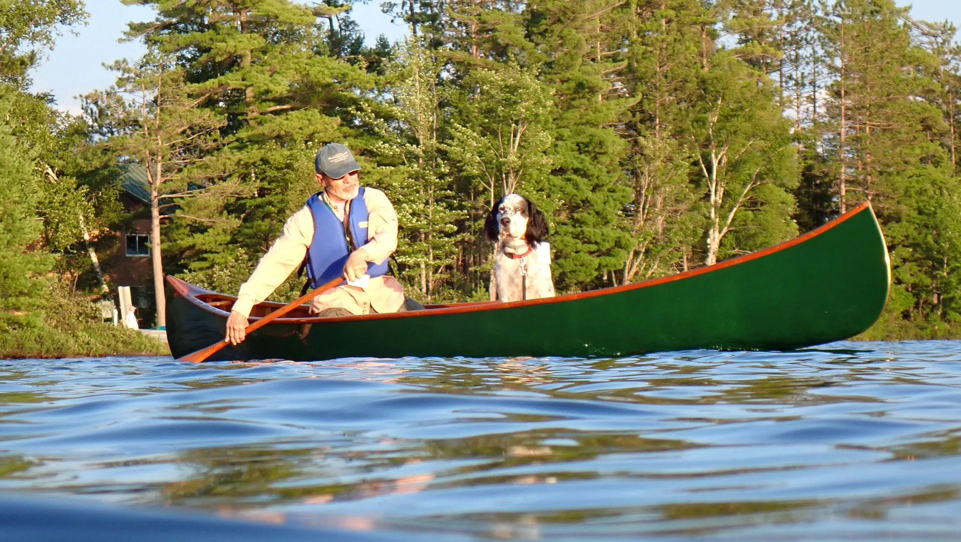 A man and his black and white dog enjoy a paddle in a green canoe.