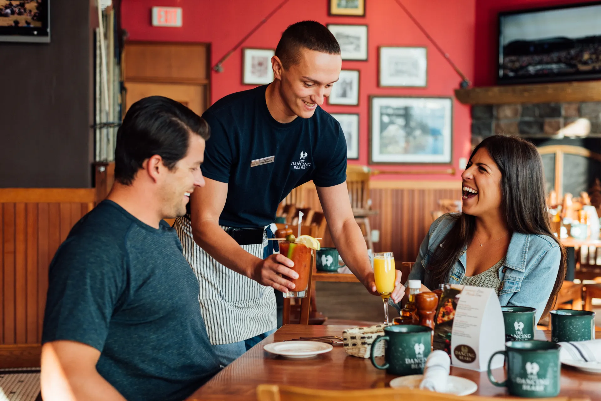 Waiter serves a mimosa and Bloody Mary to couple at table in red dining room