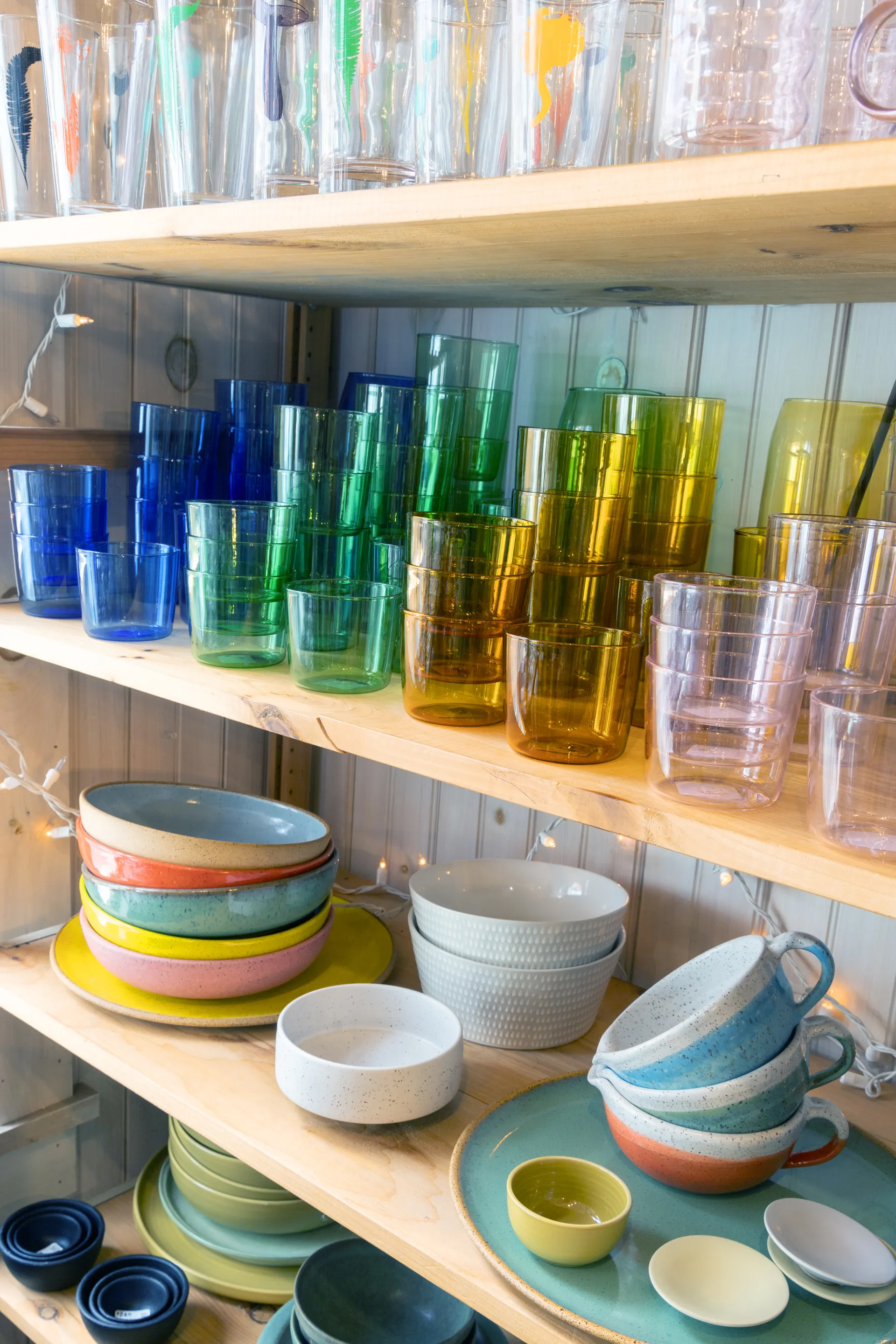Glasses and bowls in a  wide range of colors fill multiple shelves.