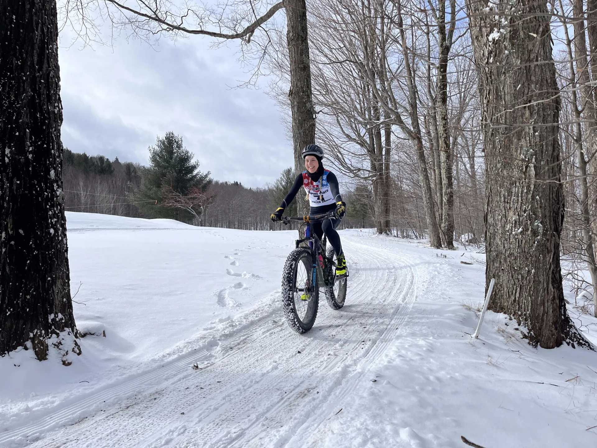 A person smiling while riding a fat-tire mountain bike on a groomed, snowy trail through a wintry forest. 