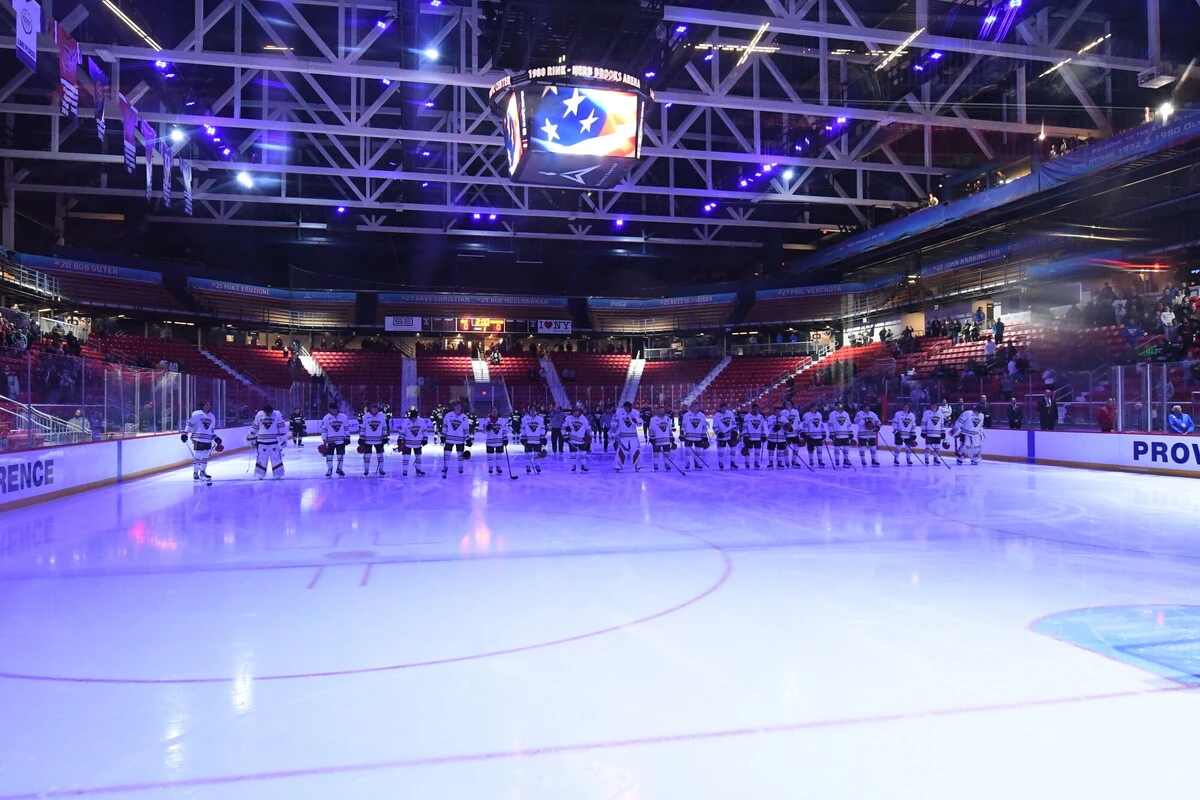 Hockey players lined up on center ice in a single file line with the ice illuminated blue in the 1980 Herb Brooks Arena