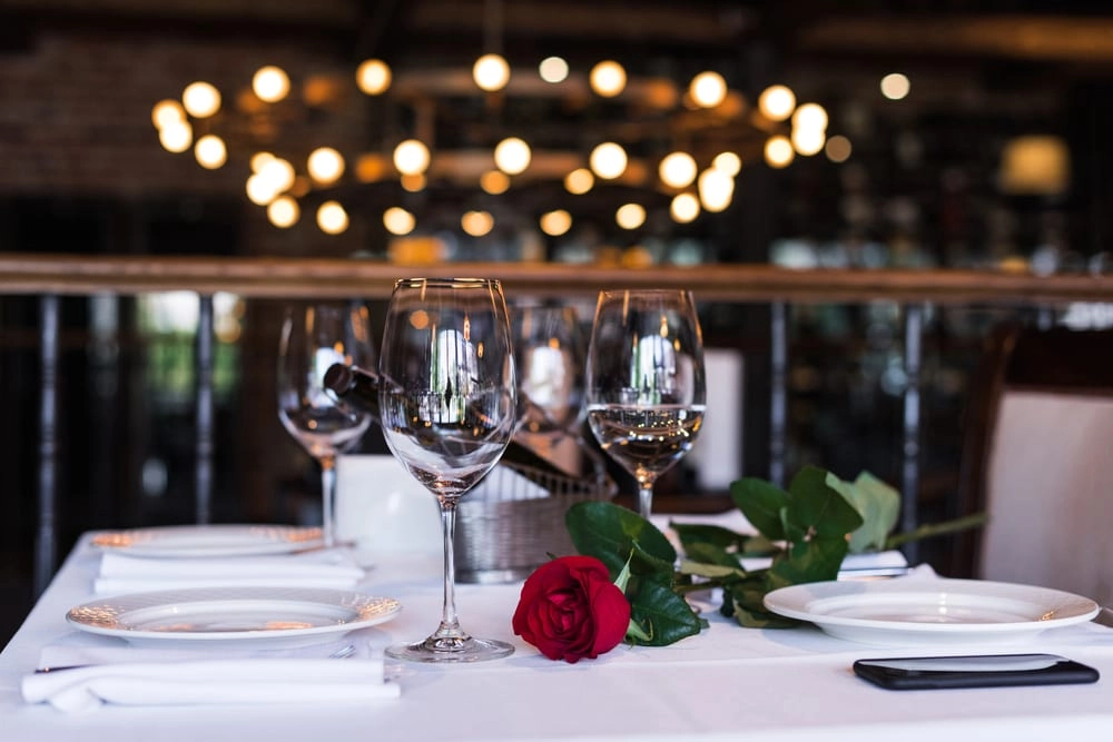 Wine glasses and a rose sit on a table with white tablecloth.
