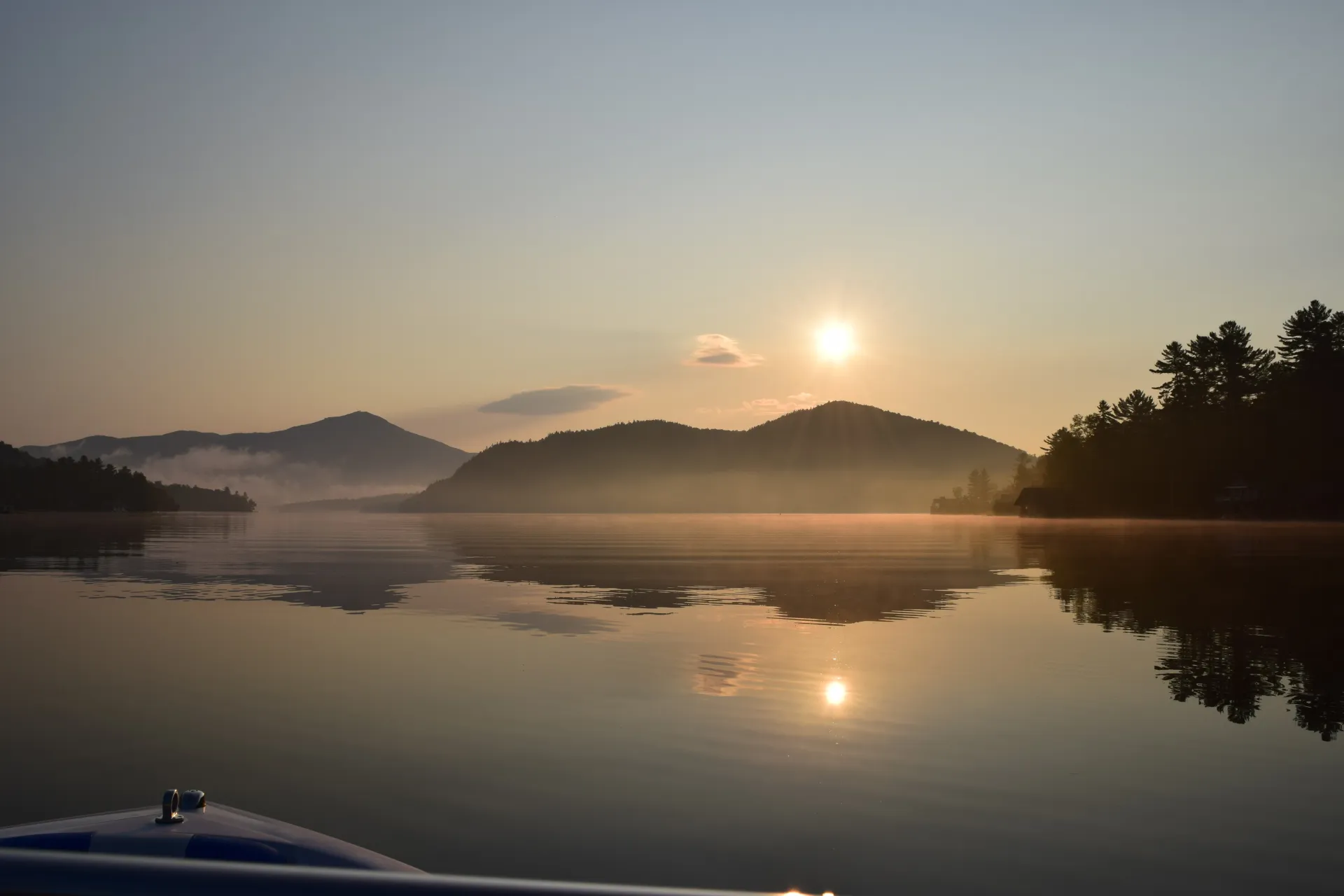 A ride on the boat on a smooth, misty lake with the mountains in the distance and the sun setting