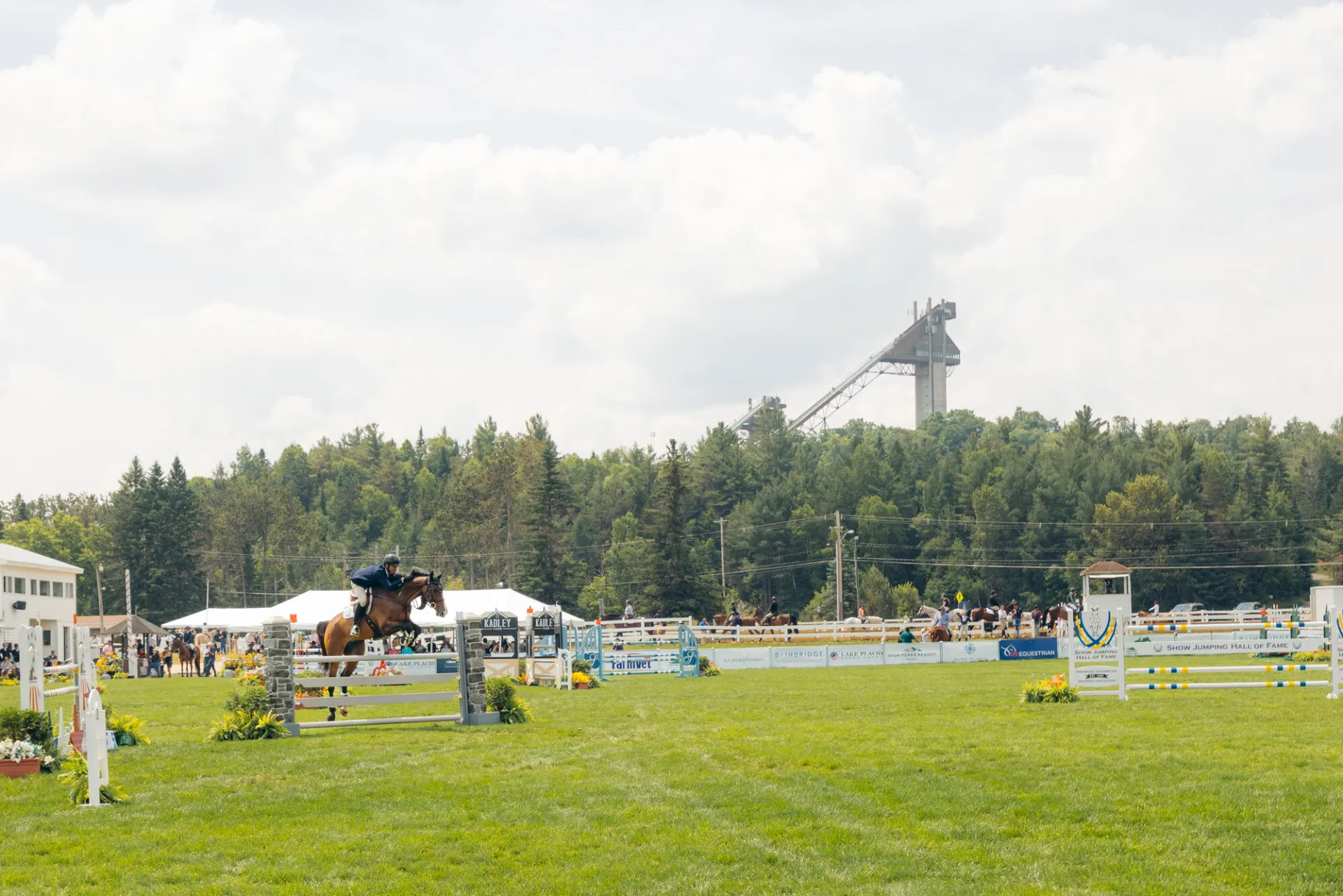 A Horse and rider jump the gates with the jumping complex ski jump over head in the background.