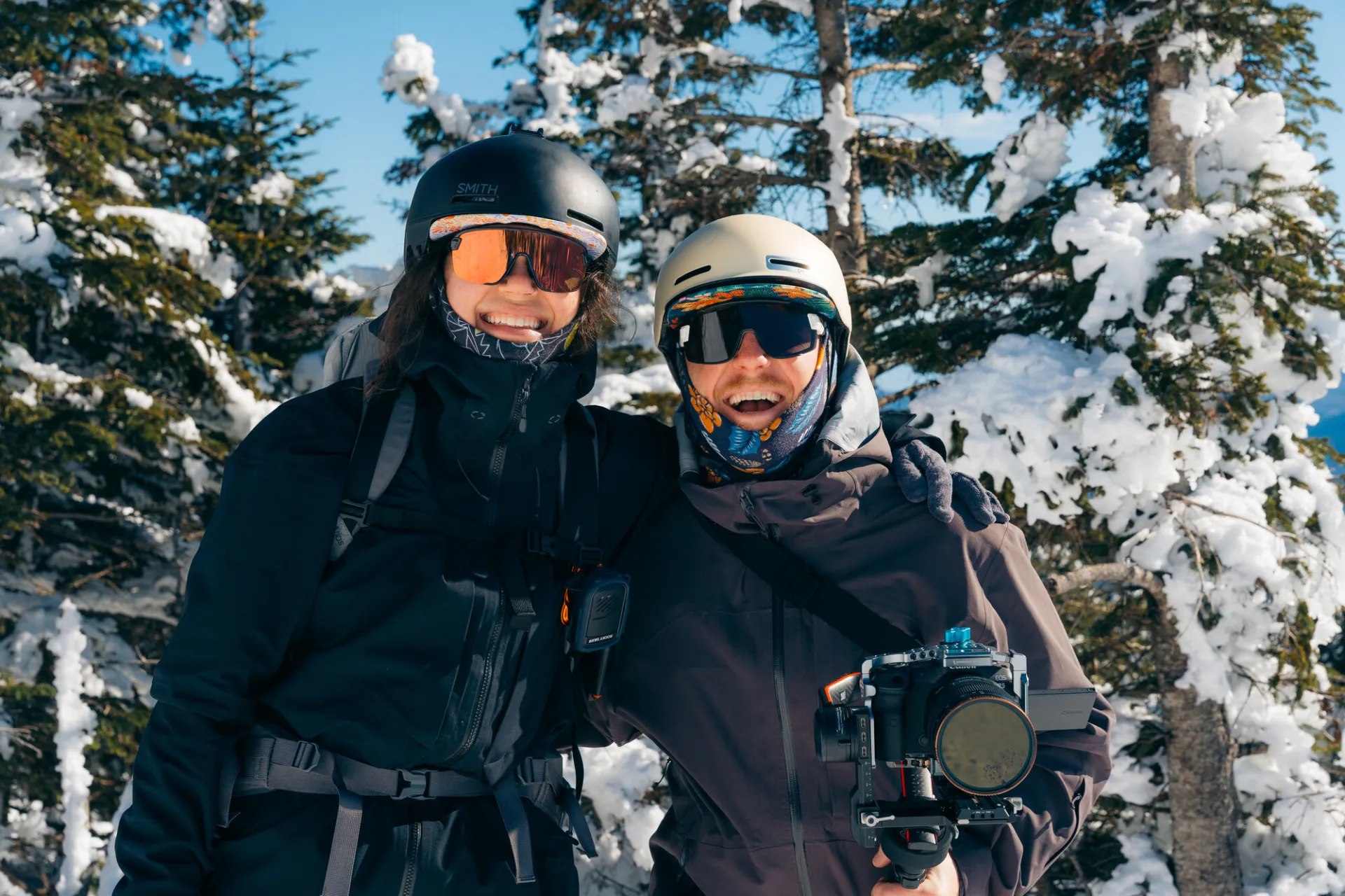 a couple bundled up for adventures in the cold smiles at the camera in front of a wintery scene