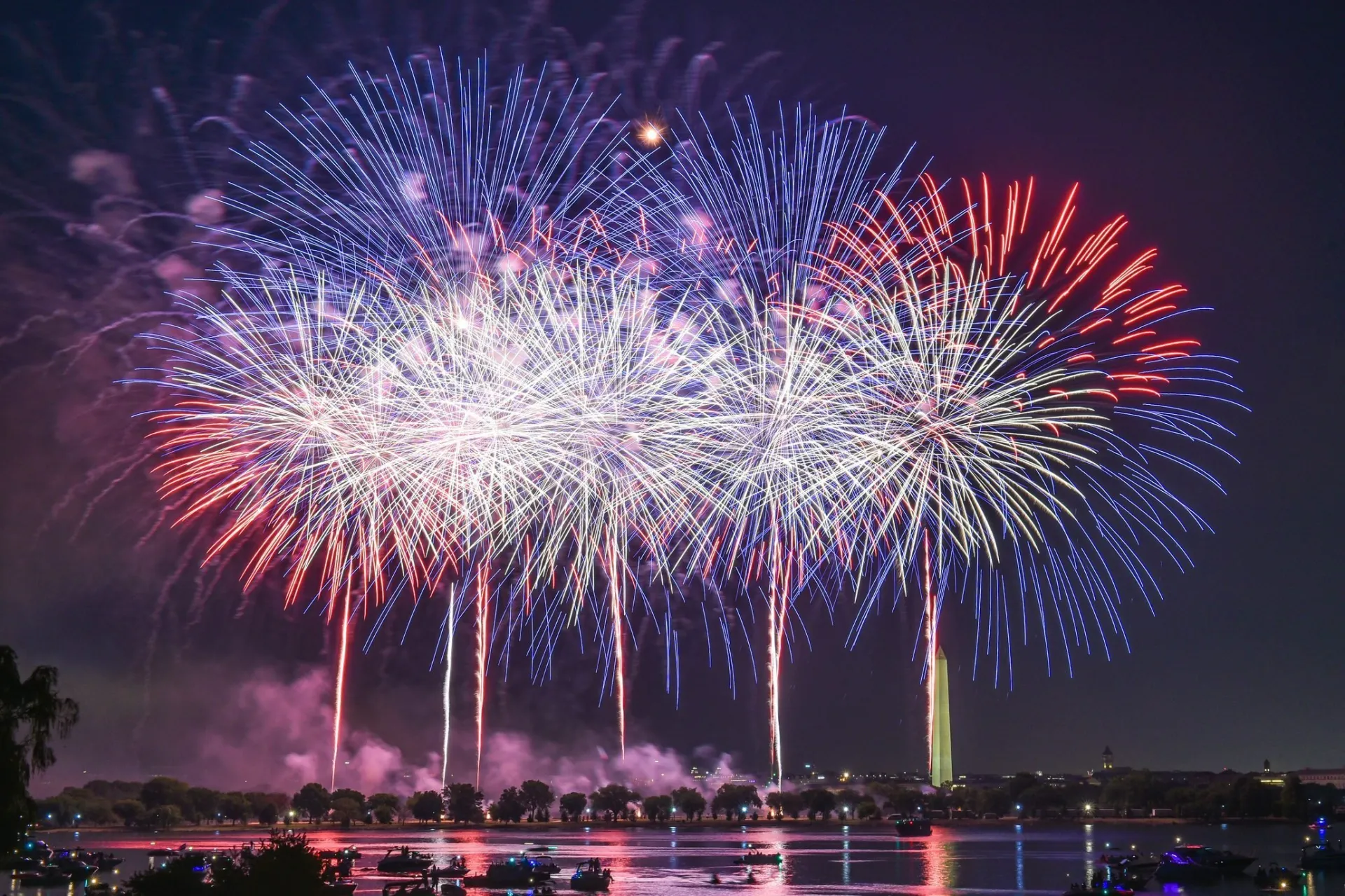 A vibrant fireworks display over a body of water, with the Washington Monument visible in the background.