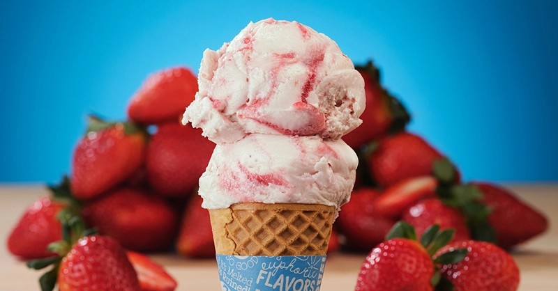 Double scoop of creamy strawberry ice cream in a waffle cone with blue background and ringed with red juicy strawberries
