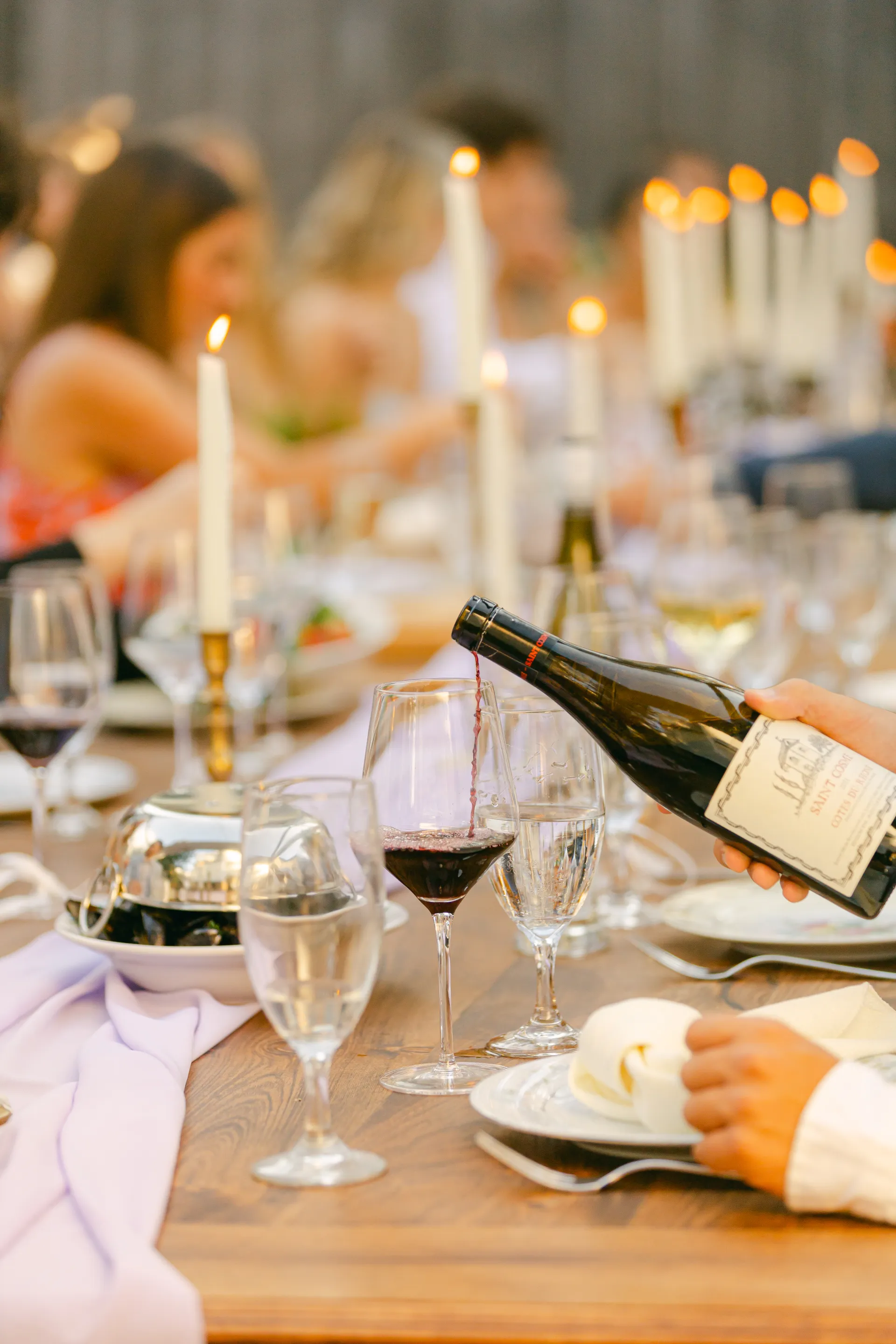 Pouring a glass of red wine on a well appointed table with lit white candles.