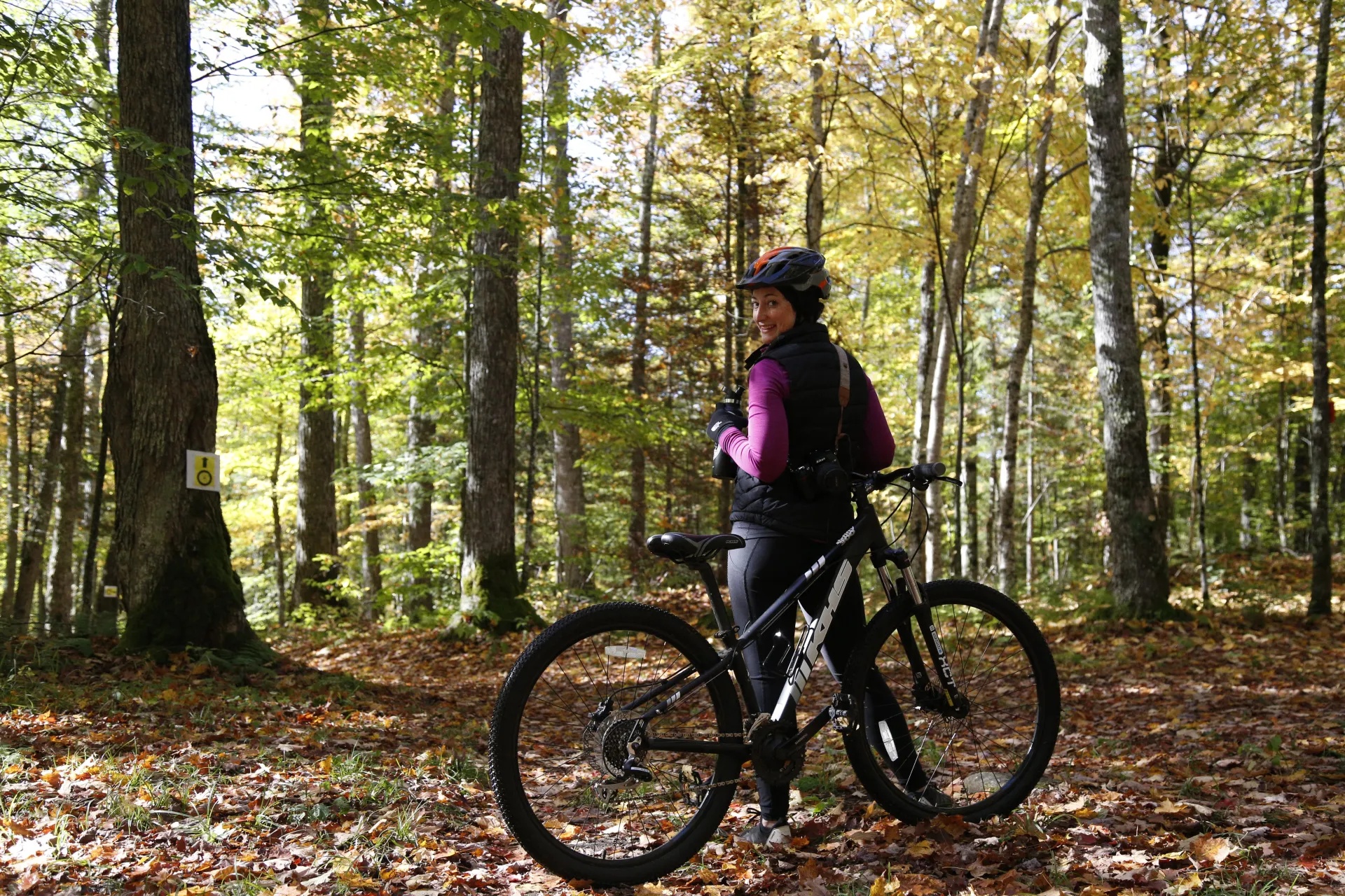 "Female smiling at the camera with a Lake Placid mountain bike rental surrounded by fallen leaves