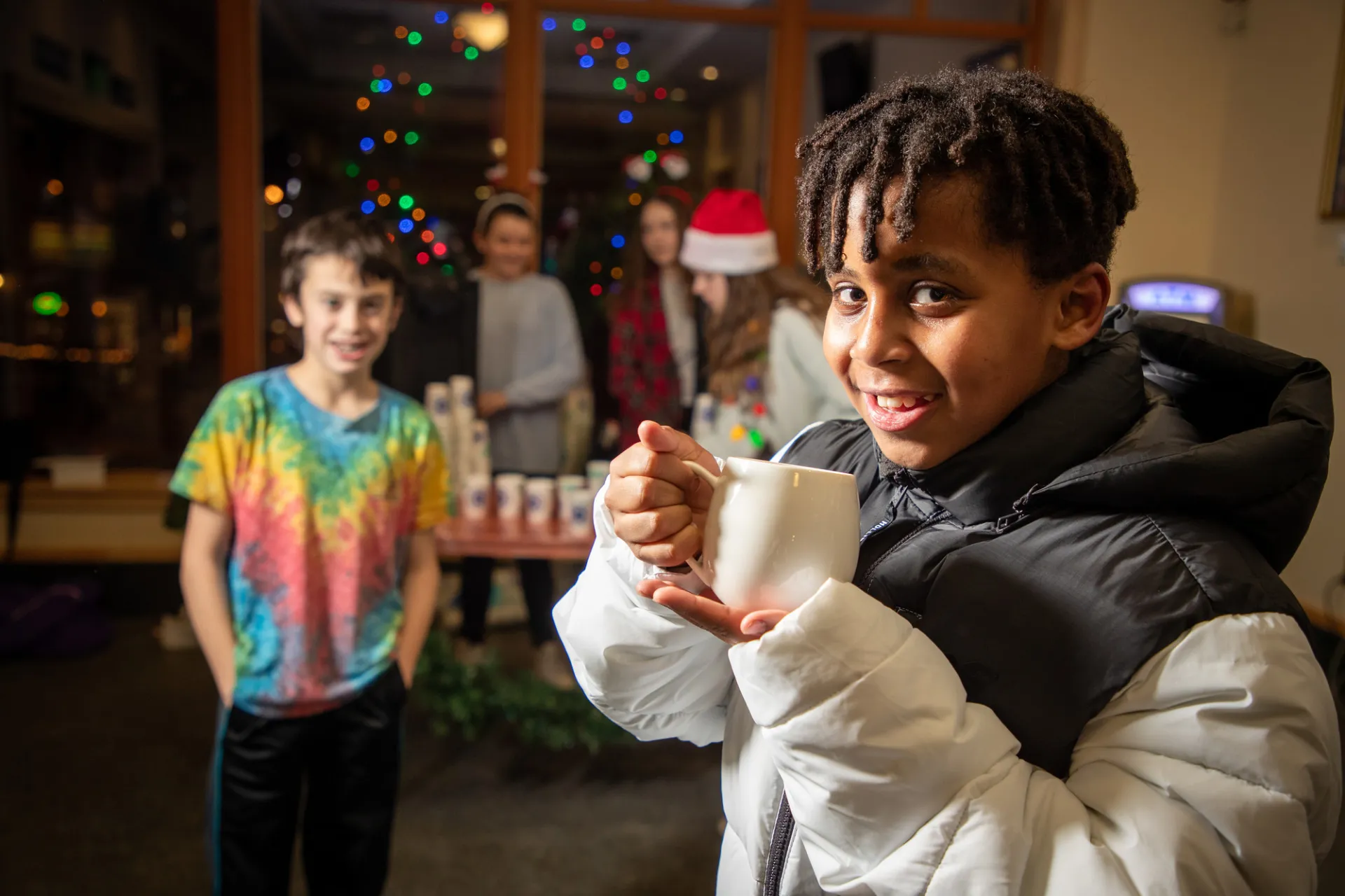 A child sips a hot cocoa with his friend behind him. 