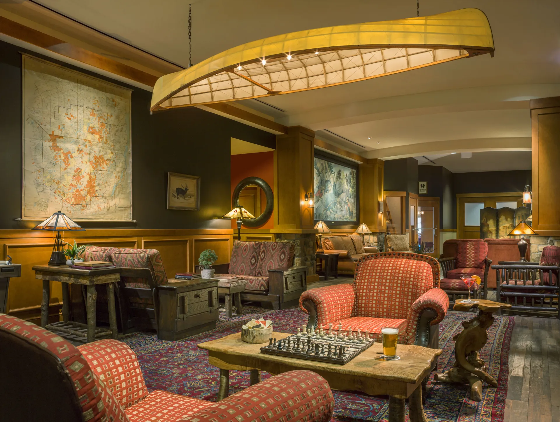 Sitting area in hotel lobby with red cushioned arm chairs, coffee table with chess set, and a canoe hanging from the ceiling