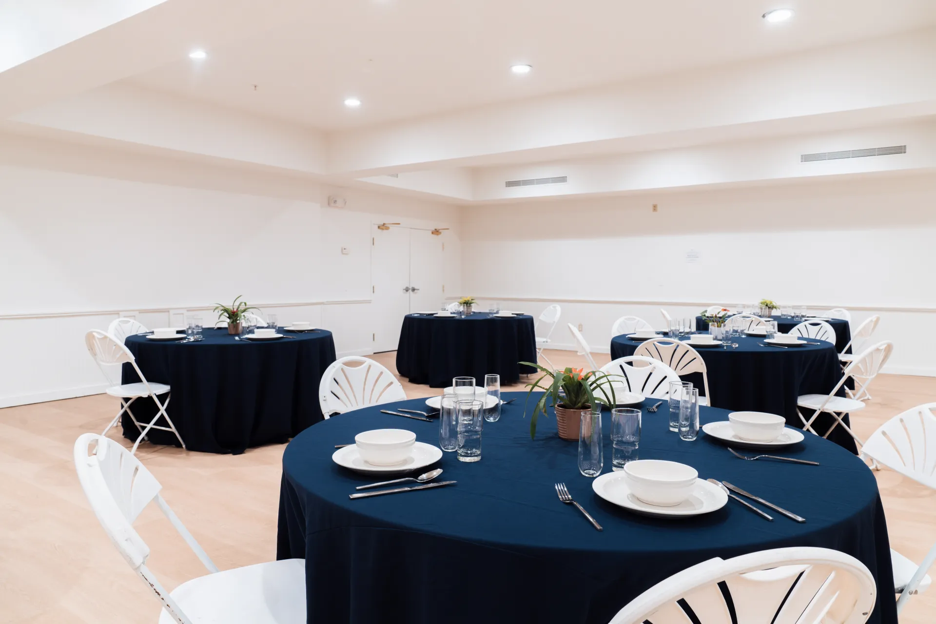 A bright and open space with round tables with deep blue cloths.