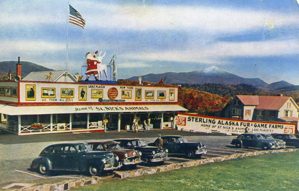 Postcard depicting Sterling Alaska Fur & Game Farms in Lake Placid, New York, showing the building with a Santa Claus and reindeer on the roof, several cars parked in front, and a mountain in the background.