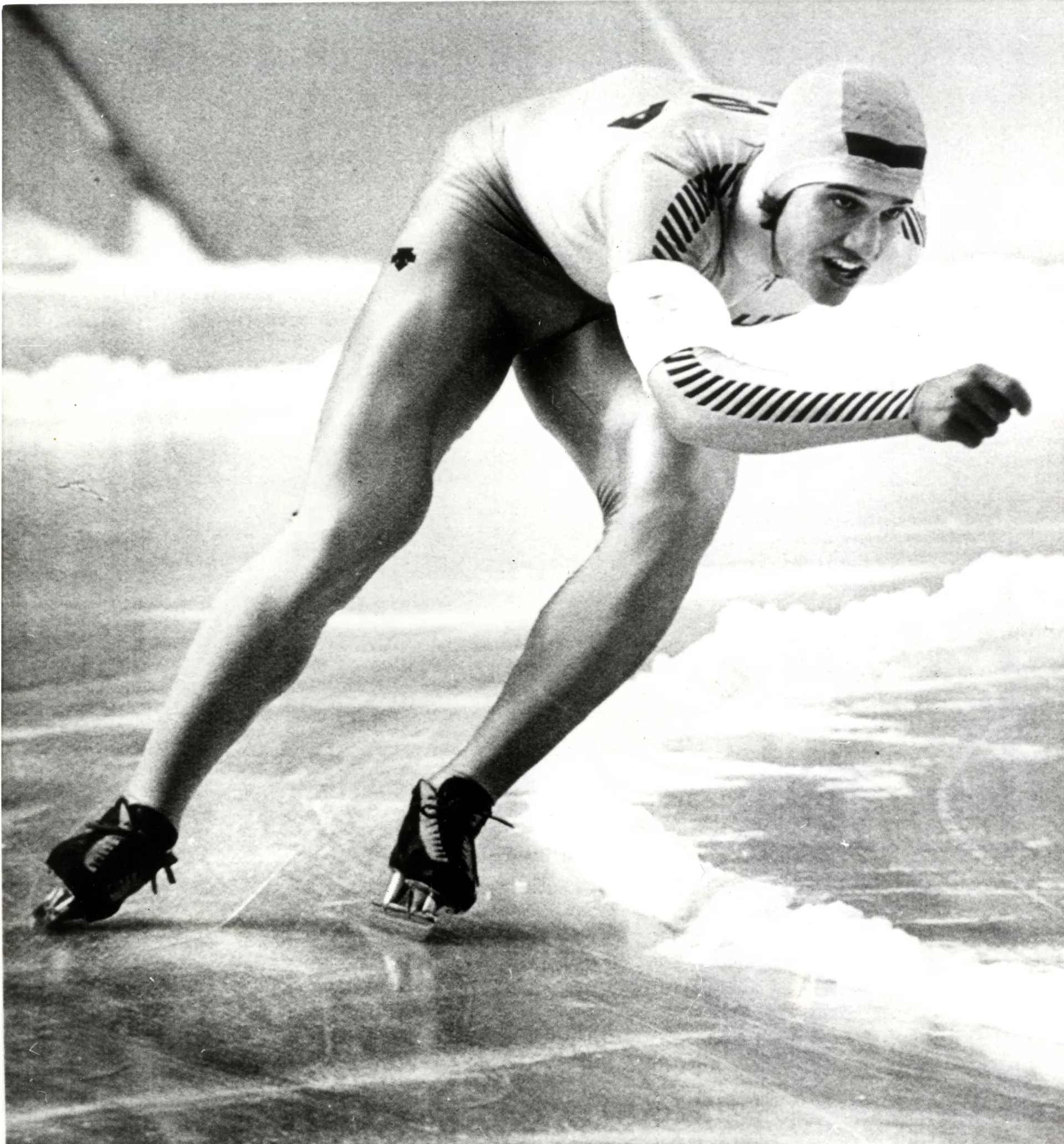 A black and white image of a male speedskater racing on an outdoor track.