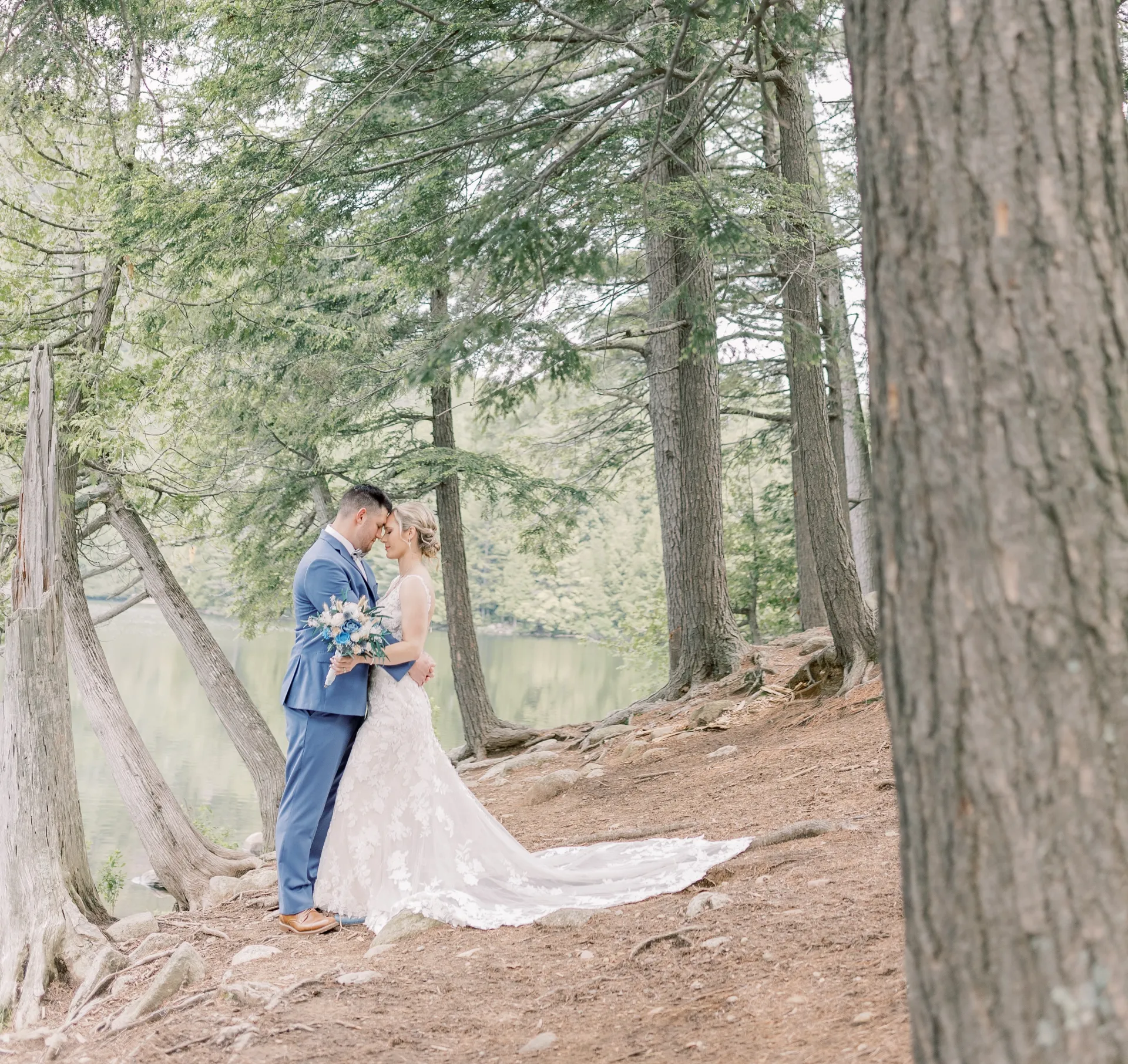 Bride and groom embrace surrounded by cedars next to a tranquil pond