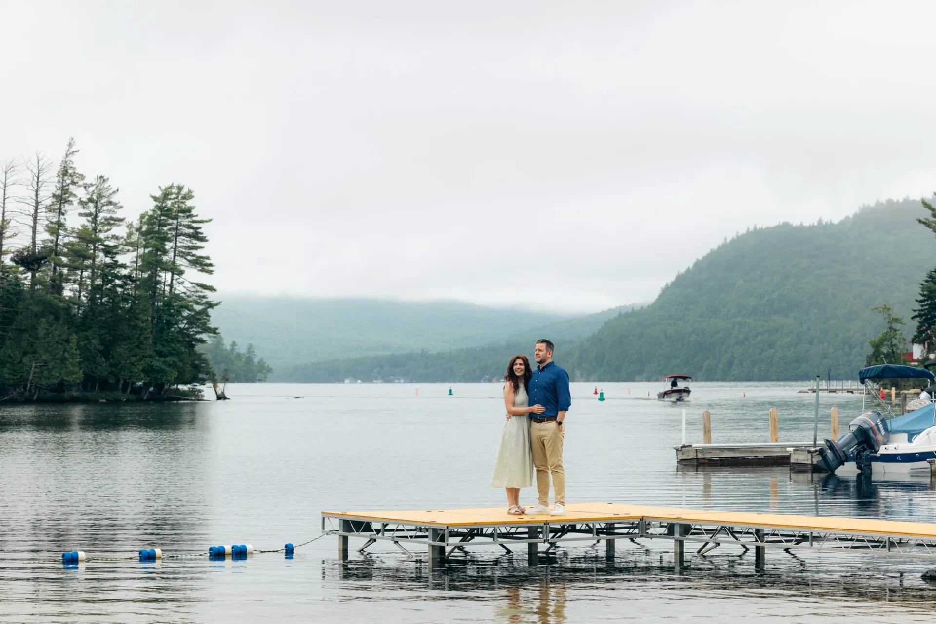 Couple stands on dock of a misty Adirondack lake in summer