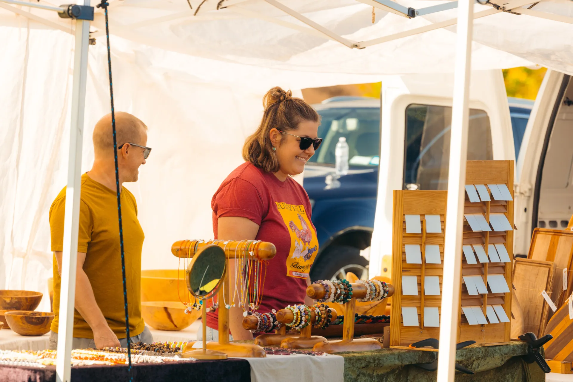 Man and woman browse table of jewelry under white tent at farmers market
